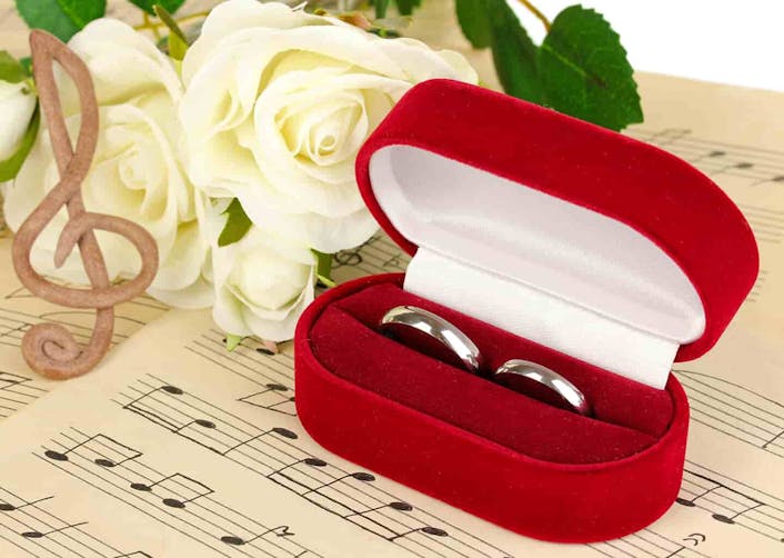 Müzik notalarının olduğu bir kağıt üzerinde; kırmızı bir yüzük kabı ve içerisinde iki adet alyans bulunuyor. Yüzük kutusunun solunda beyaz güller ve nota şekli verilmiş aksesuar bulunuyor.