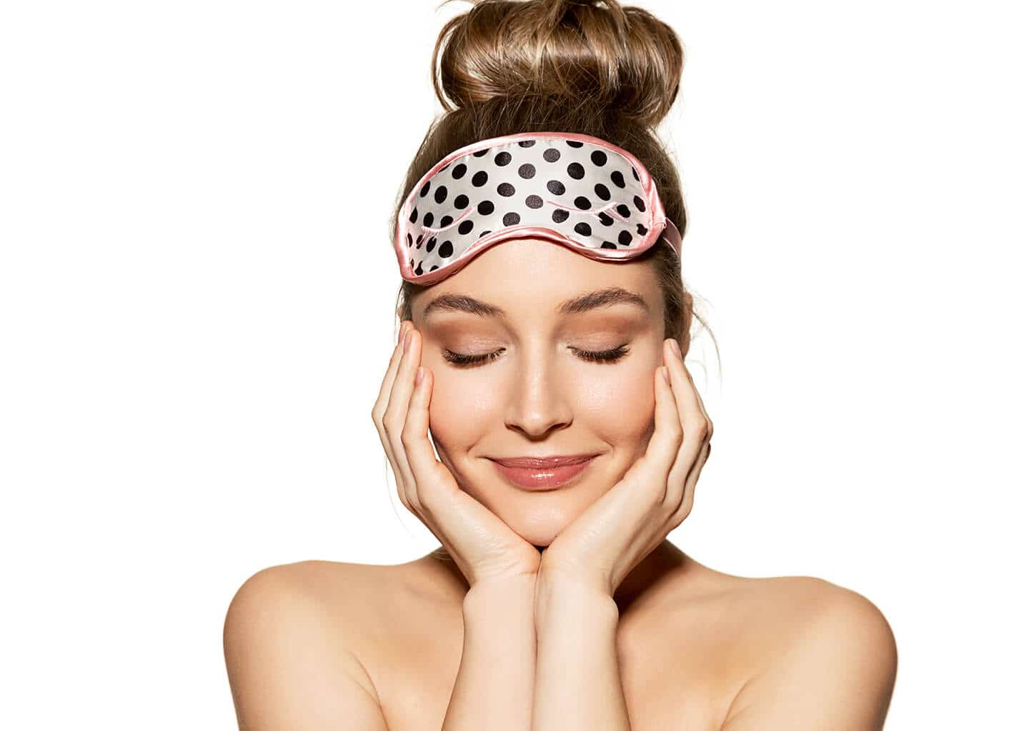 Yakın plan çekimde genç kadın gözleri kapalı bir şekilde yanaklarından tutuyor. Saçları topuz olarak toplanmış kadının kafasında uyku bandı bulunuyor.