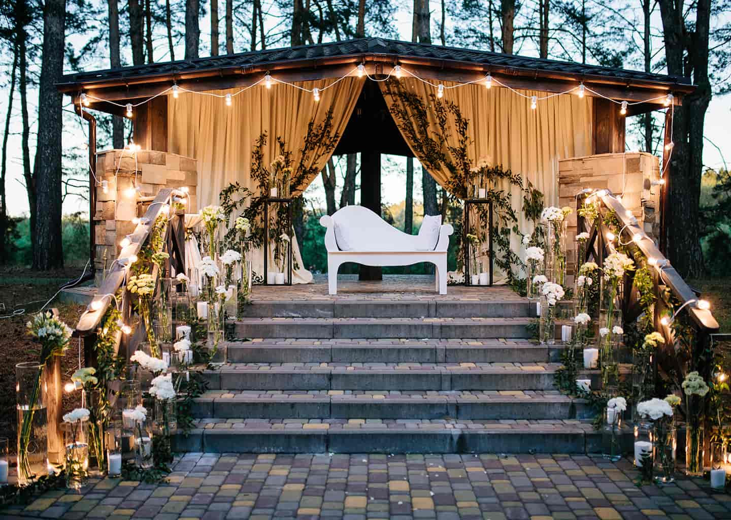 Ormanlık bir alan içerisinde 6 basamağı bulunan merdivenin sonunda, açık renk perdeleri olan bir ev bulunuyor. Evin önünde beyaz renk bir koltuk duruyor.