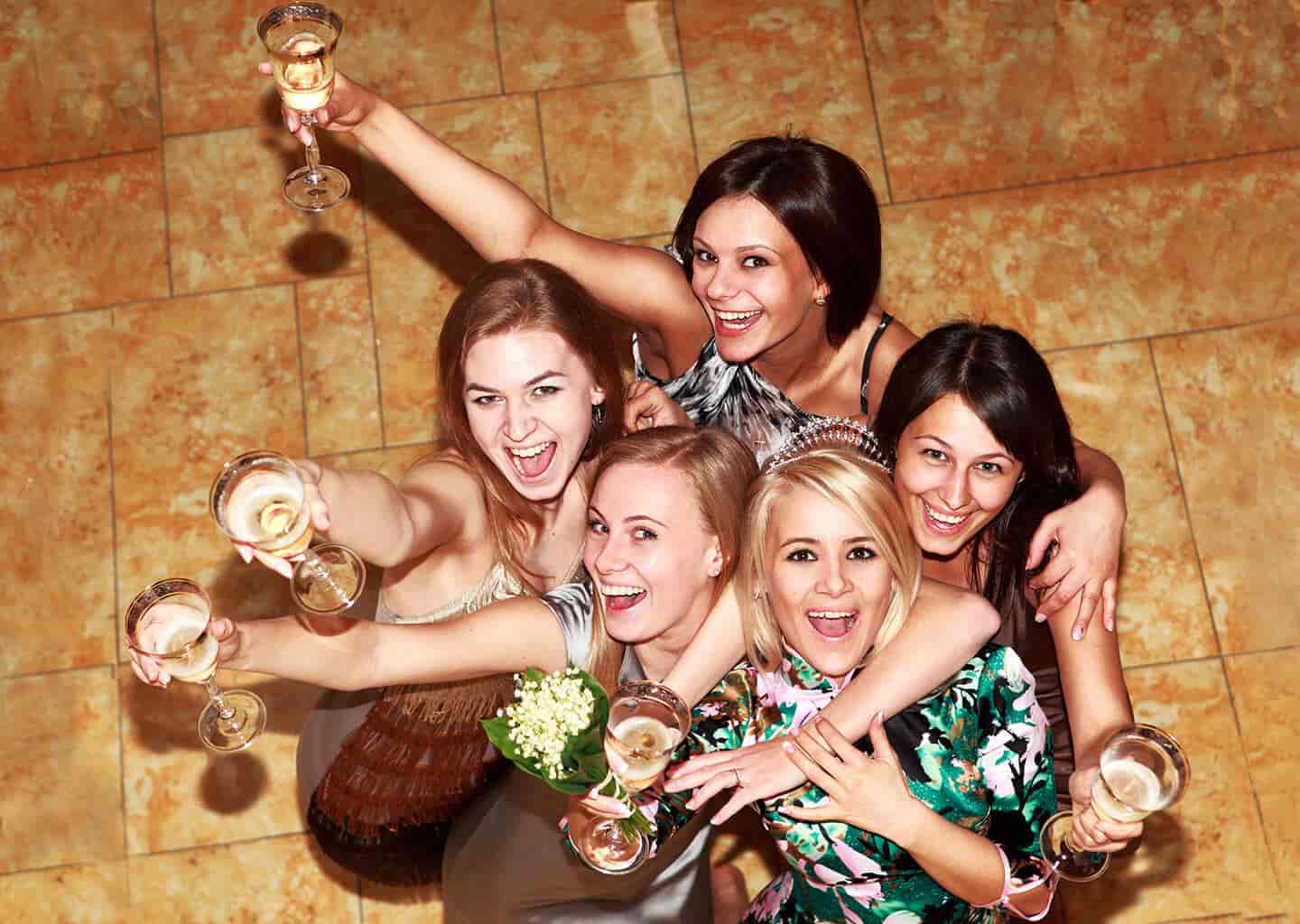 5 kadın yukarı doğru bakarken kadehlerini havaya kaldırarak gülümsüyorlar.