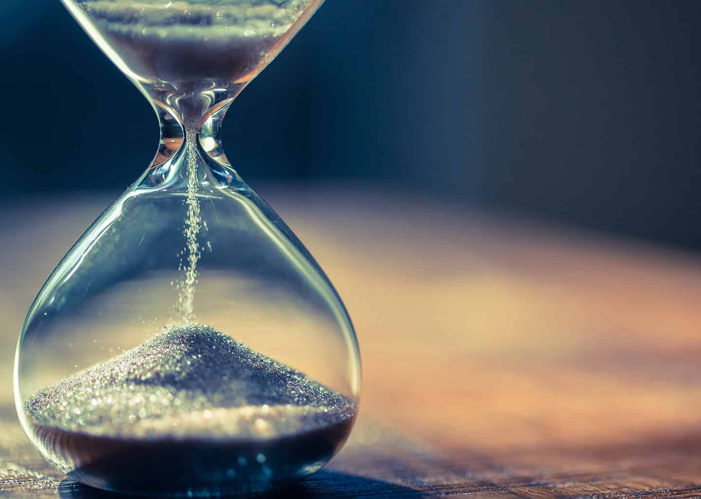 Yakın plan çekimde; koyu renk arka plan önünde bir kum saati bulunuyor.