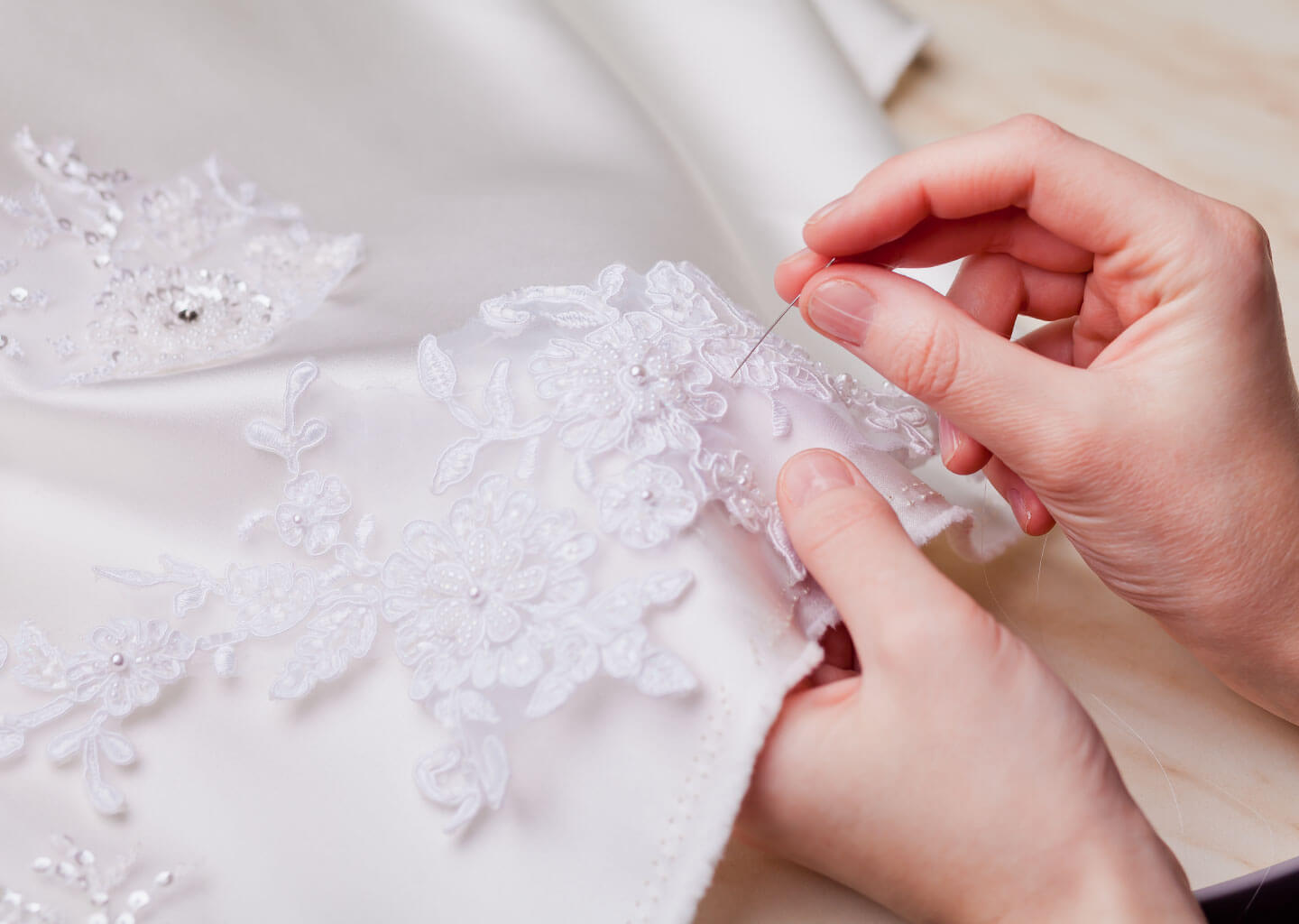 Yakın plan çekimde kadın gelinliğin eteğine dantel işleme dikiyor.