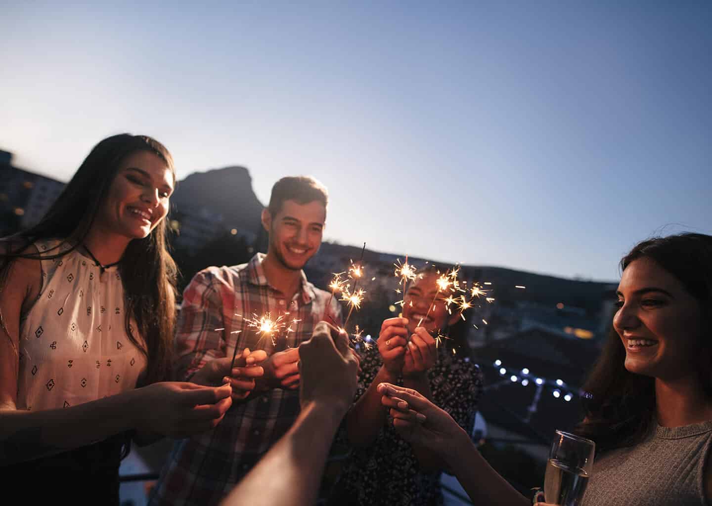 Balkonda kutlama yapan arkadaş grubu, elinde yıldız saçan tutuyor ve gülümsüyorlar.