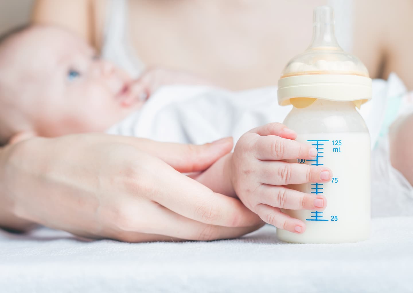 Yakın plan çekimde kadın bebeğini kucağında tutuyor. Bebeğin eli ise bir biberonun üzerinde duruyor.