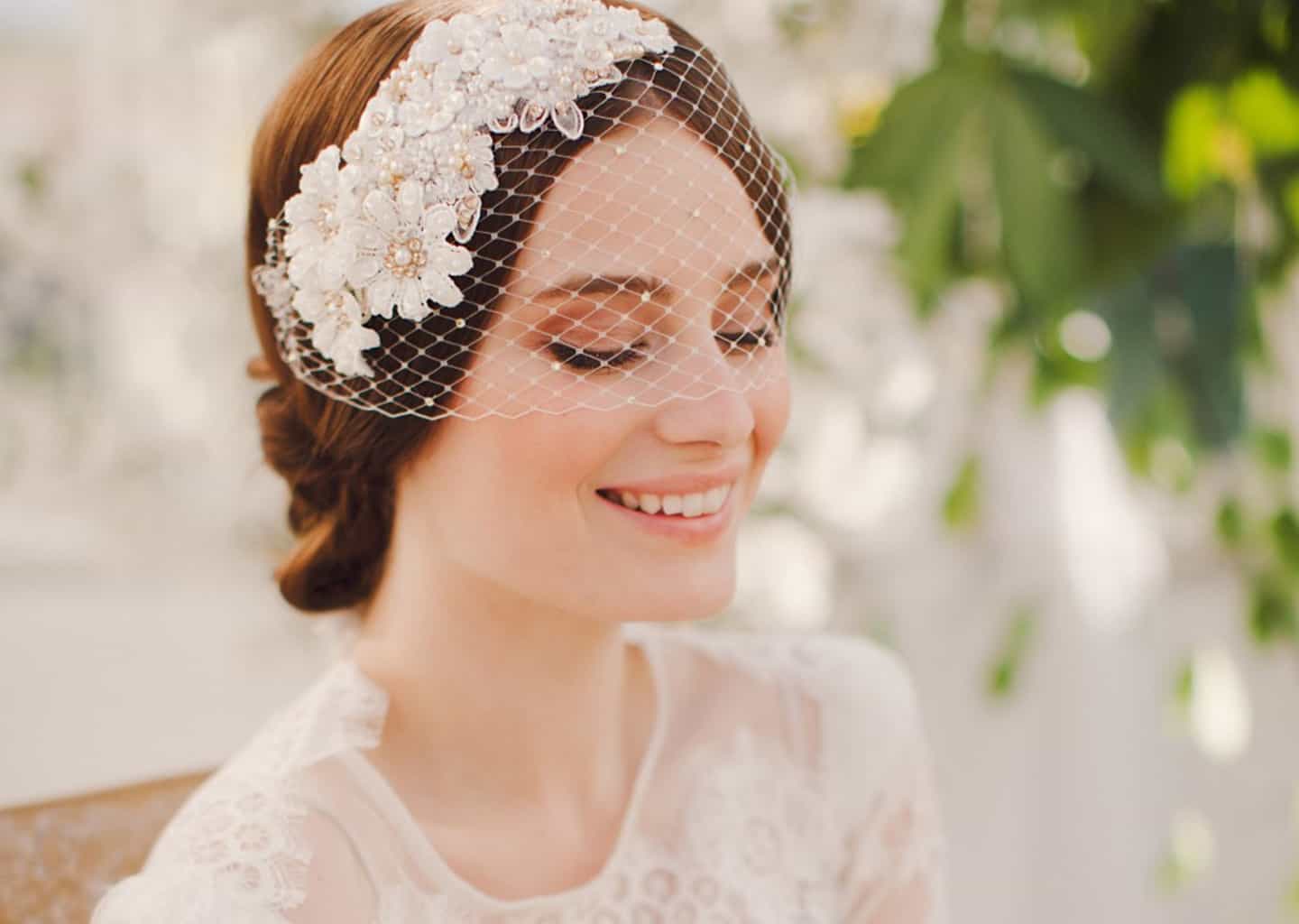 Yakın plan çekimde gelinin başında yüzünün yarısına kadar uzanan ve çiçek desenleri olan bir duvak bulunuyor. Gelin gözleri kapalı duruyor ve gülümsüyor.