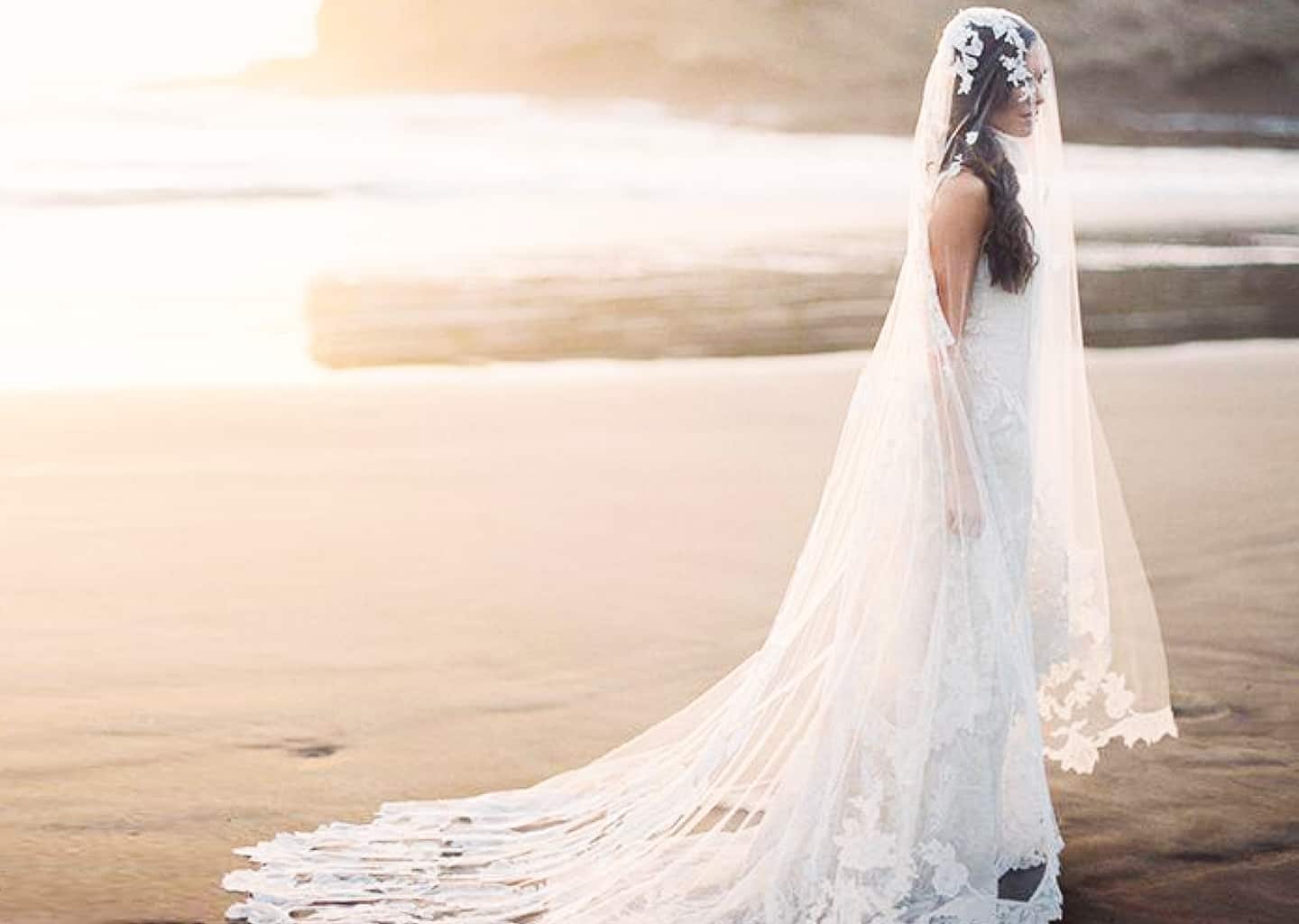 Plajda olan gelin, denize arkası dönük bir şekilde duruyor. Gelinin üzerinde dantel işlemeli bir gelinlik ve kafasında uzun bir duvak bulunuyor.