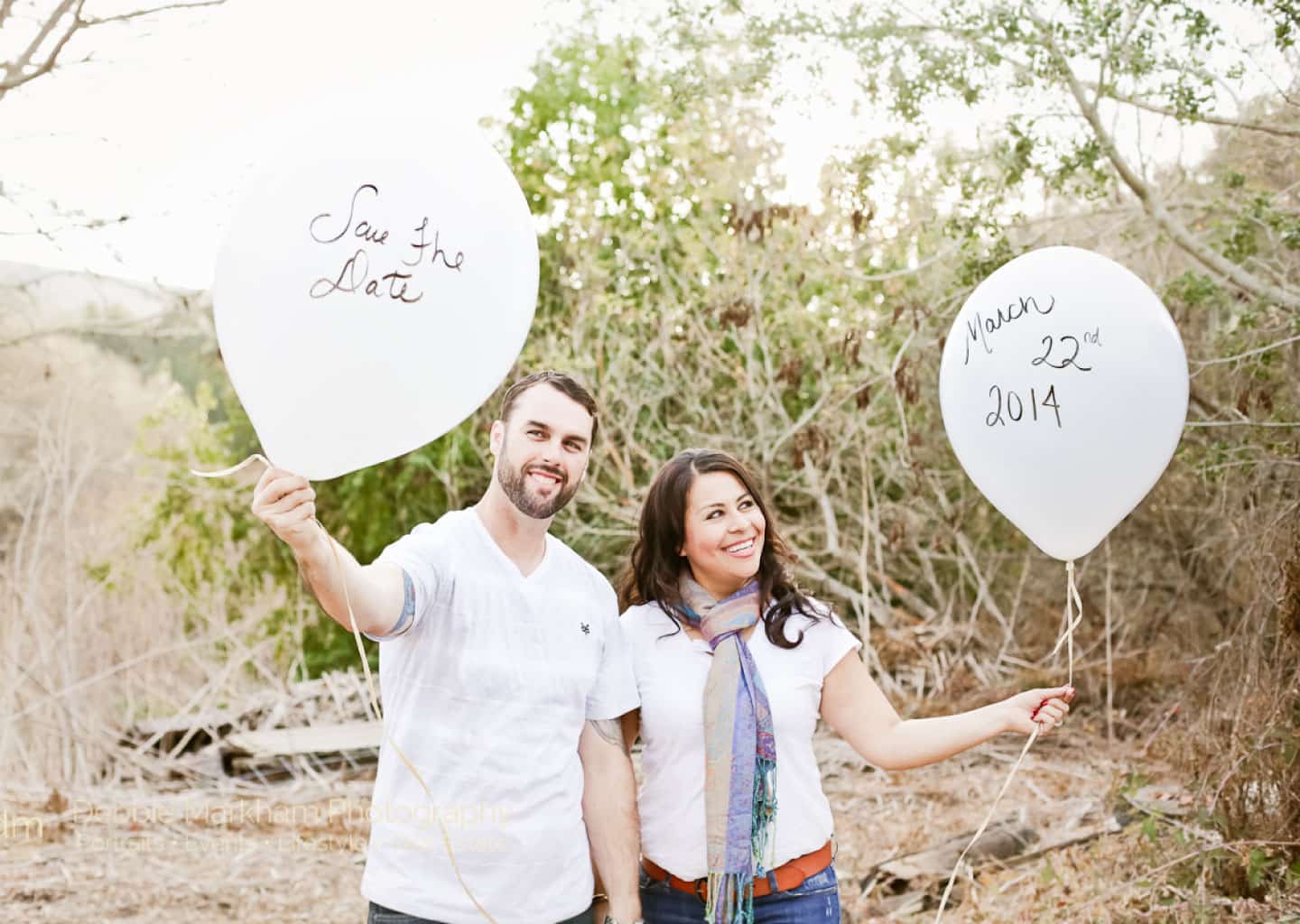 Ormanlık bir alan içerisinde kadın ve adam yan yana dururken, ellerinde tarih ve isim yazan balonlar tutuyorlar. Adam ve kadın gülümsüyorlar.