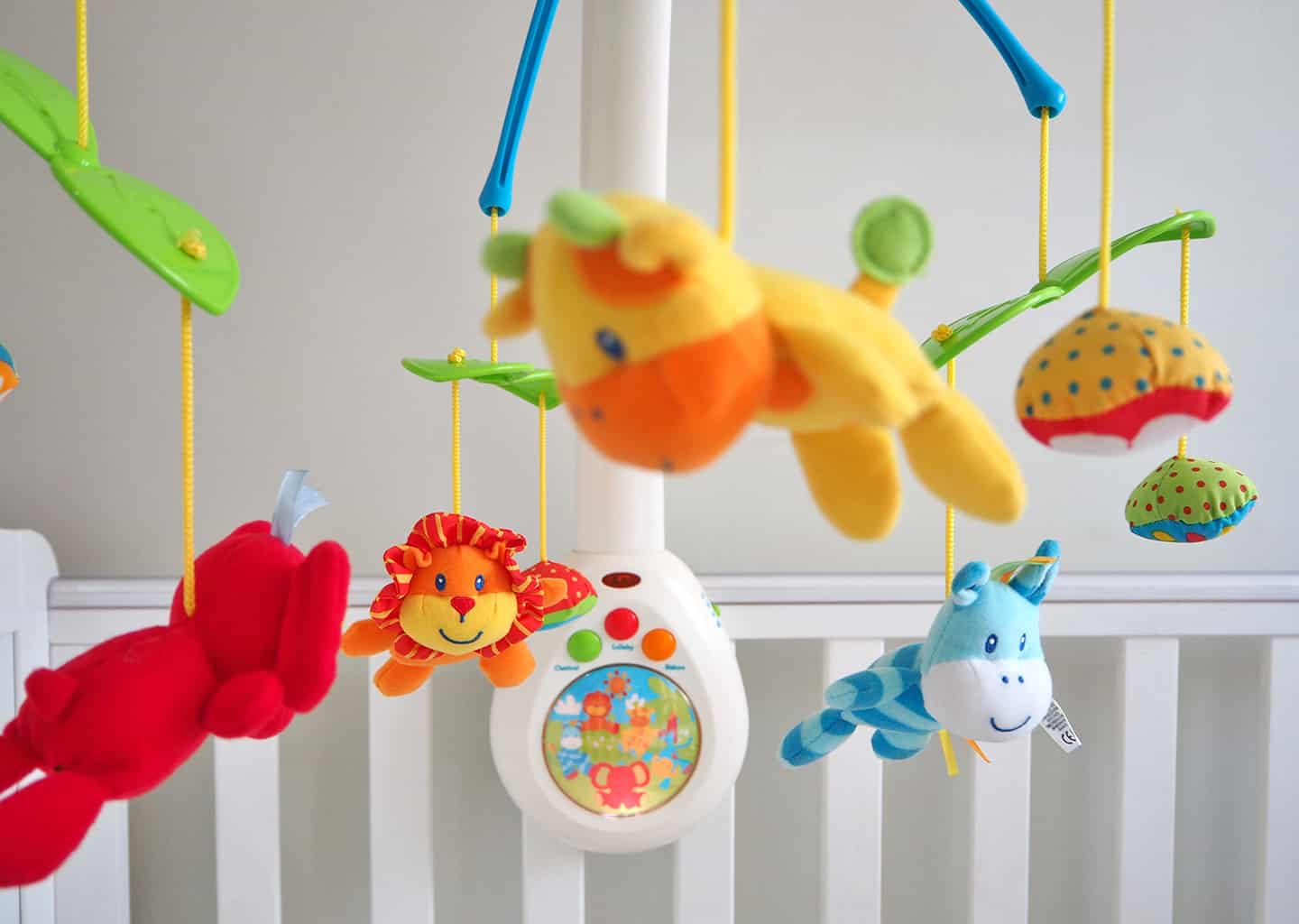 Yakın plan çekimde bebek yatağının üzerinde havadan yatağa doğru sarkan farklı hayvanlardan yapılmış bebek oyuncağı bulunuyor.