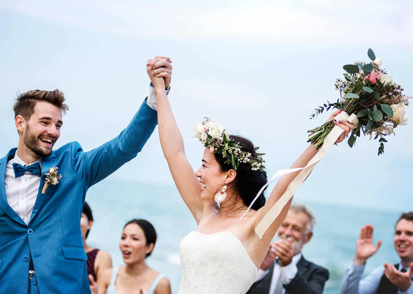 Gelin ve damat el ele tutuşurken kollarını havaya kaldırıyor ve gülümsüyorlar.