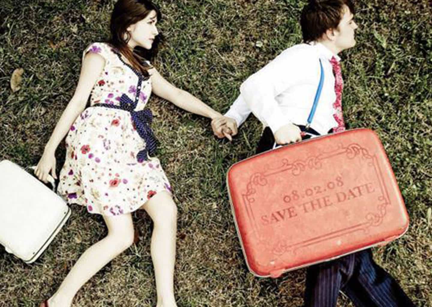 Çimlerin üzerine bir şekilde uzanmış olan kadın ve adam, ellerinde valiz tutuyor.