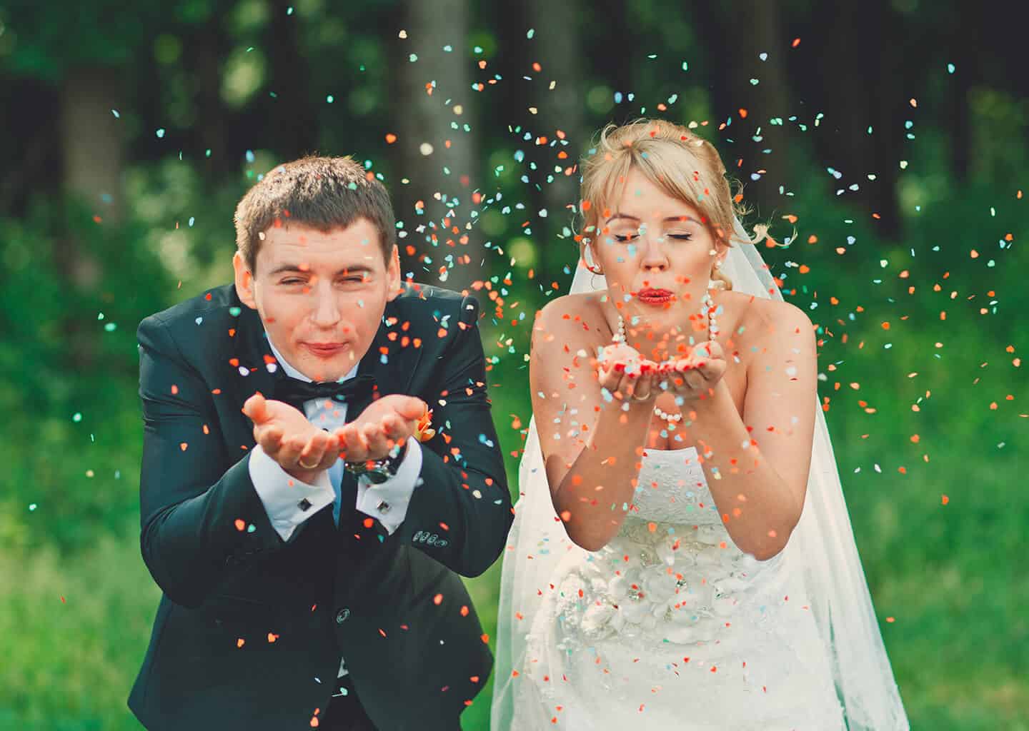 Gelin ve damat gözleri kapalı bir şekilde ellerinde bulunan konfeti parçalarını üflüyorlar.