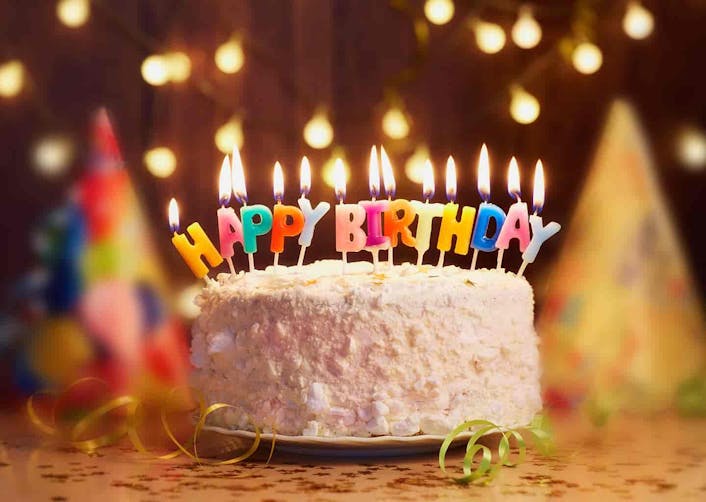 Masa üzerinde pembe bir pasta bulunuyor. Pastanın üzerindeki yanan mumlarda "Happy Birthday" yani "Mutlu Yıllar" yazıyor.