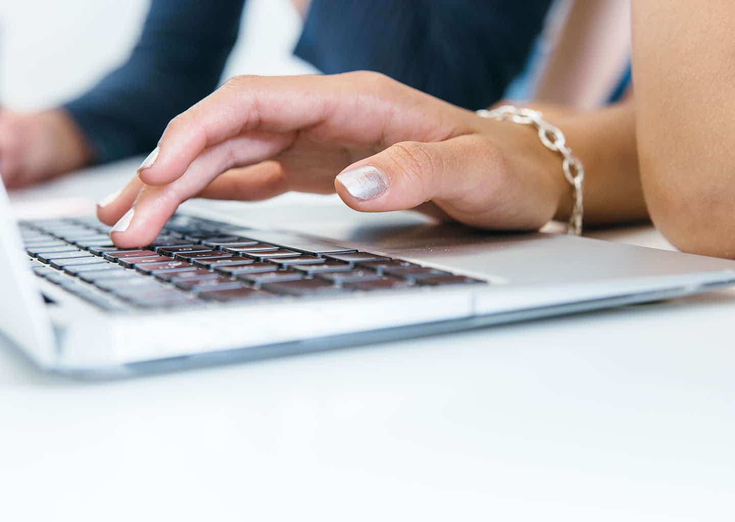 Yakın plan çekimde kadın; masada bulunan dizüstü bilgisayarın klavyesinde yazı yazıyor.