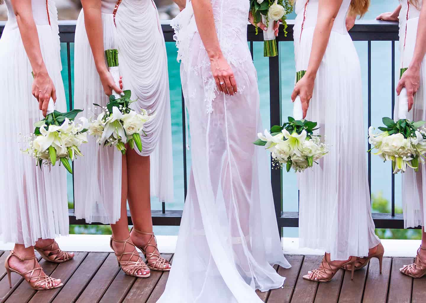 Yakın plan çekimde; gelin ve nedimeler ellerinde çiçek buketi tutuyor. Arka planda deniz manzarası görünüyor. 