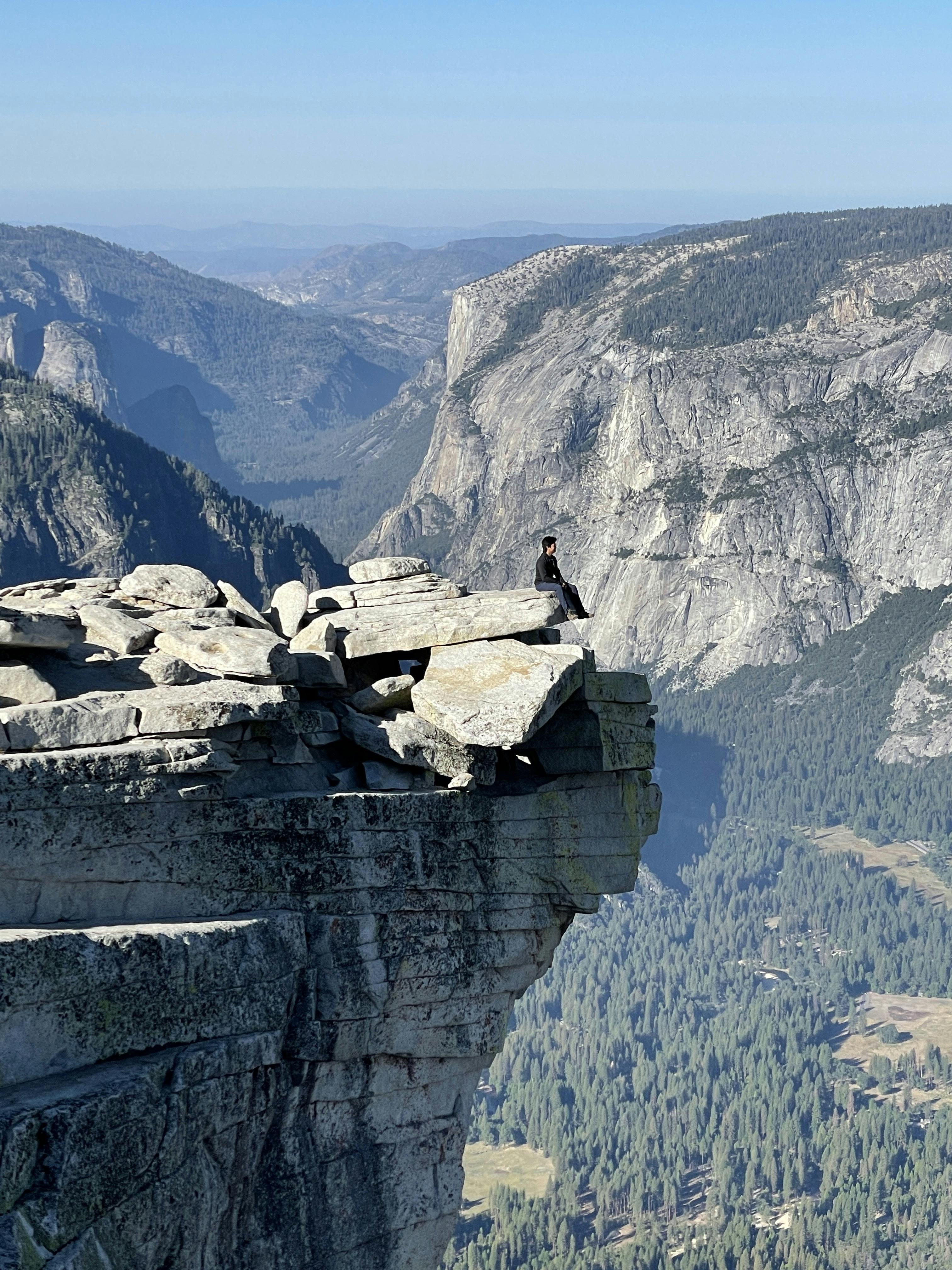 The man is sitting on the edge of the rock and looking forward 