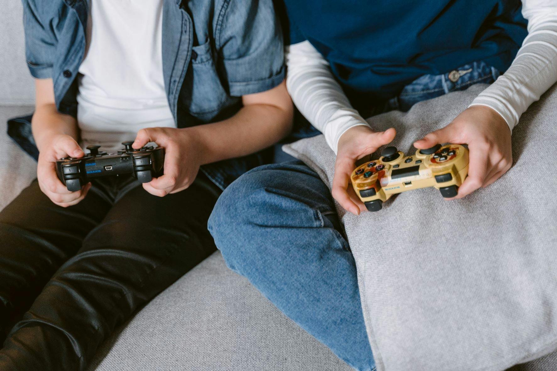 Photo of two boys playing games on a couch. Their faces are cropped out. They represent the influence of video games in transmedia storytelling, transmedia companies, and transmedia franchises
