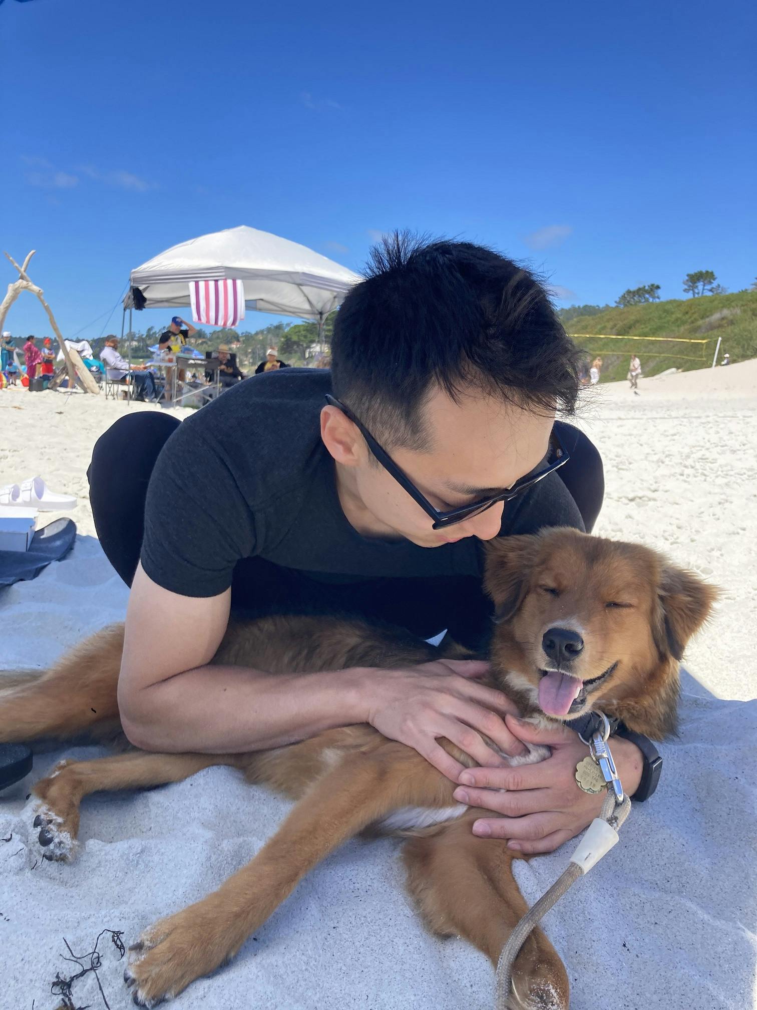 Alex on a beach with his dog Zorro. He's squatting down while petting him