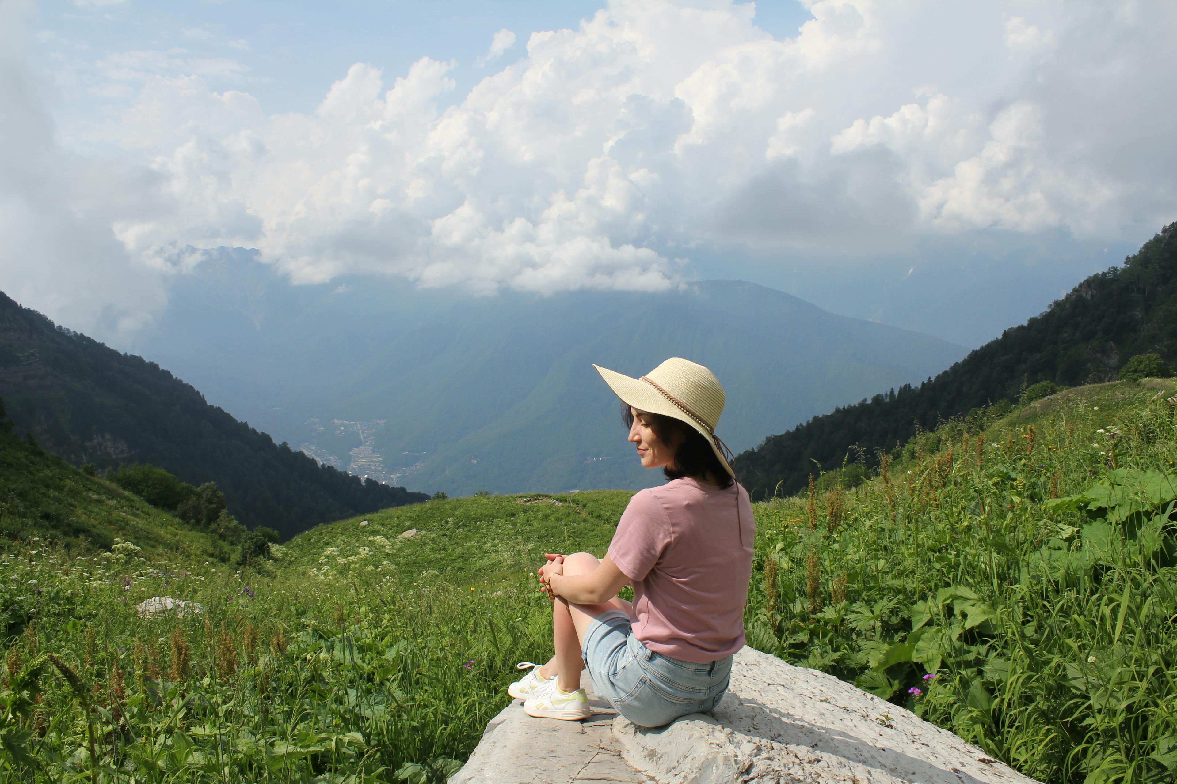 The woman is sitting on the rock with her eyes closed and surrounded by mountains
