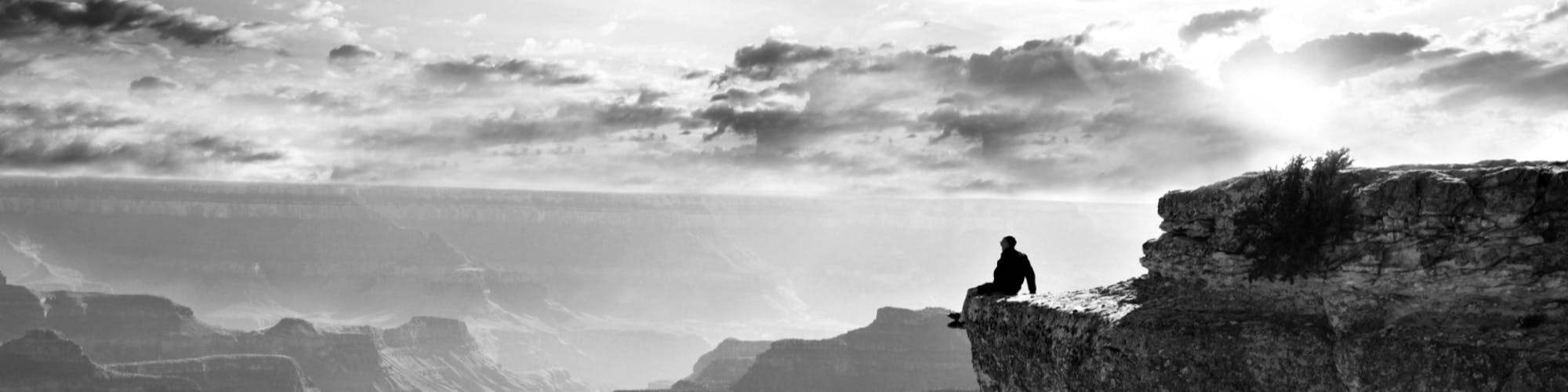 Mann sitzt auf dem Gipfel eines Berges und läßt die Beine über den Abhang baumeln