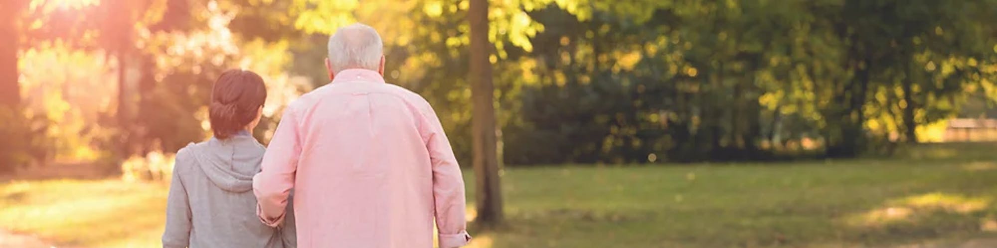 Älterer Mann hakt sich bei jüngerer Frau beim Spazieren ein