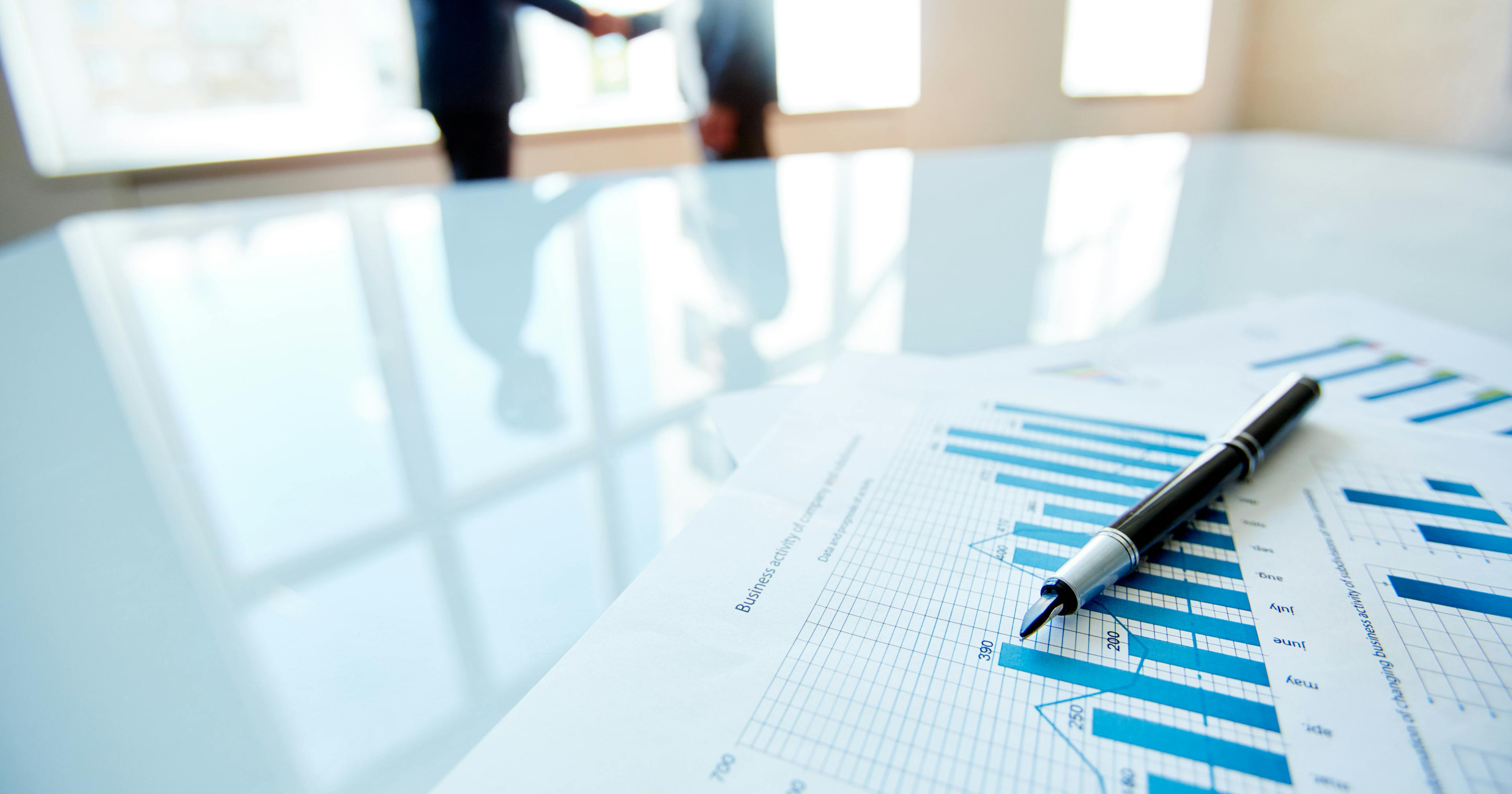 Handschlag zweier Geschäftsleute mit Diagramm Geschäftsanalyse auf Tisch im Vordergrund