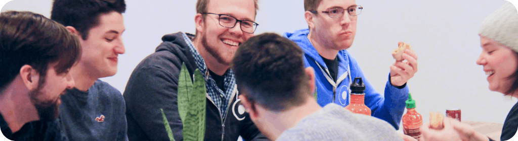 Ionic team eating food at table. A bottle of Sriracha is visible. Who's idea was that? It could possibly be Dan's, who is staring off into the distance with what looks like a half eaten uncrustable in his hand.