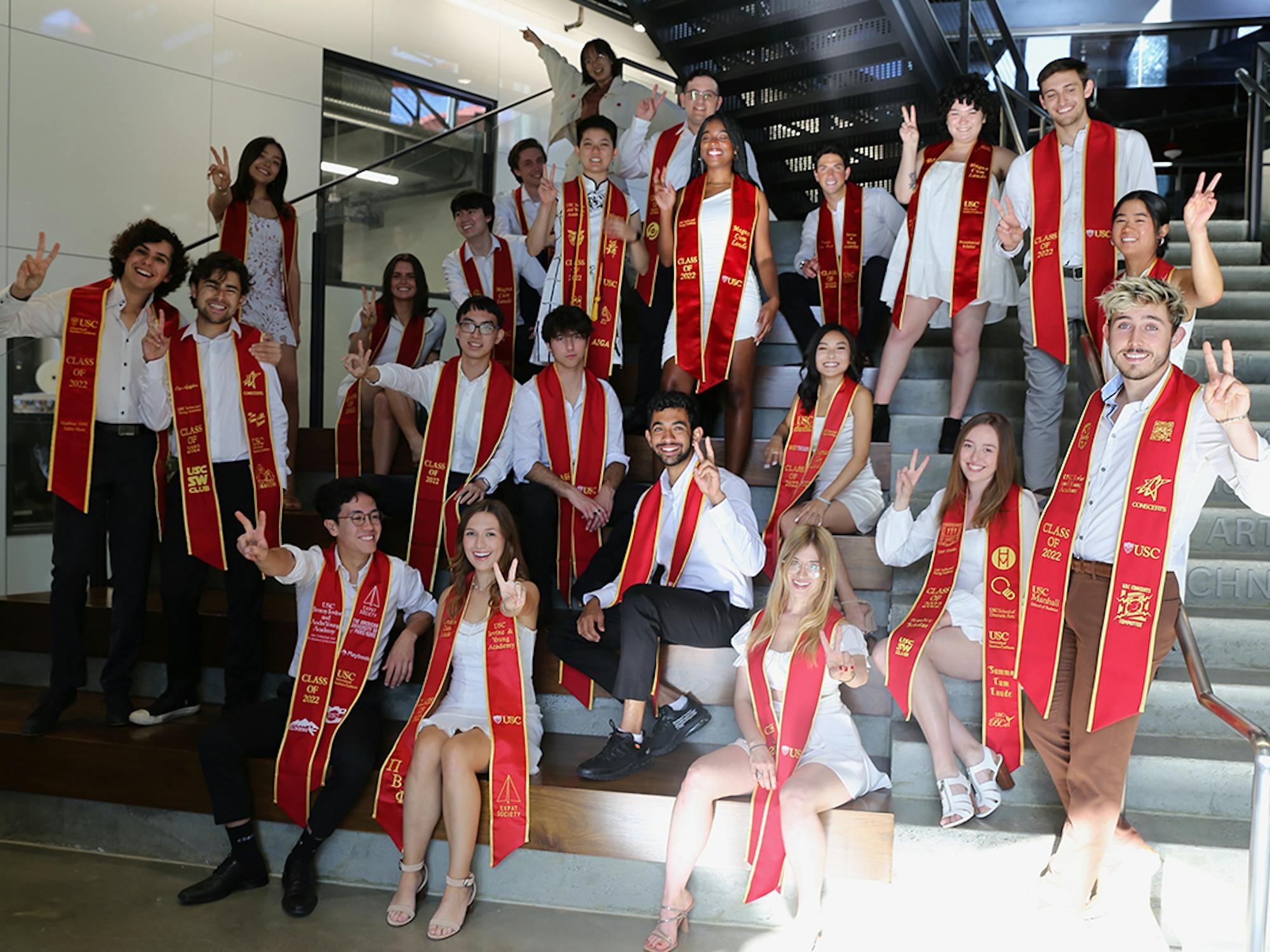 Graduating students in red sashes pose on steps
