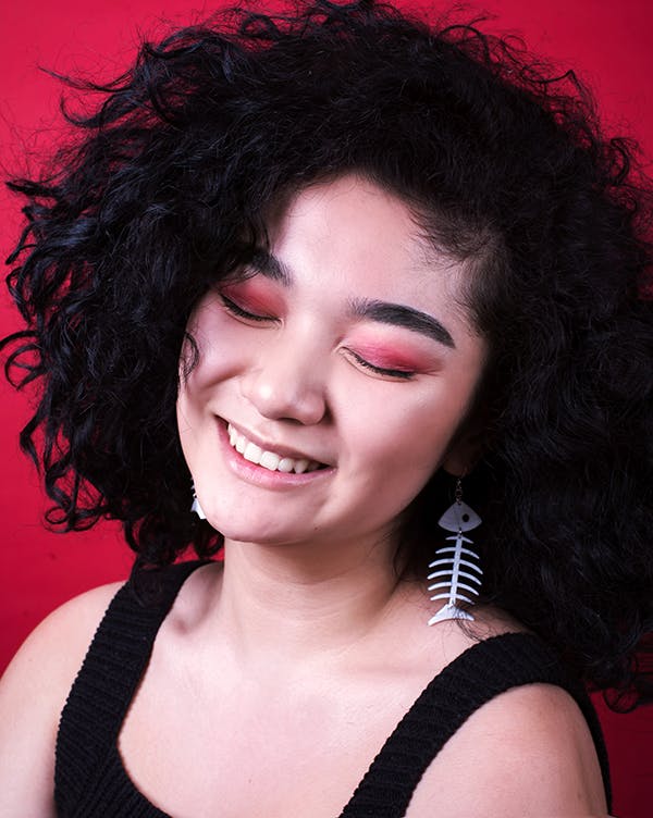 Young woman with curly black hair smiles against red background
