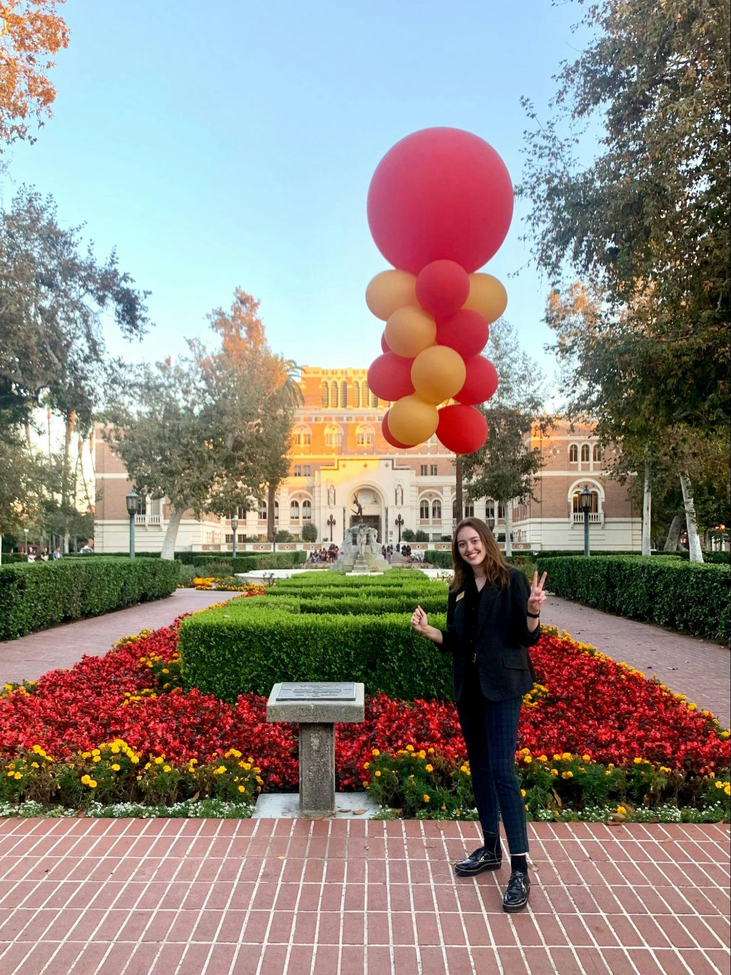 A young woman poses in front of cardinal and gold flowers and balloons