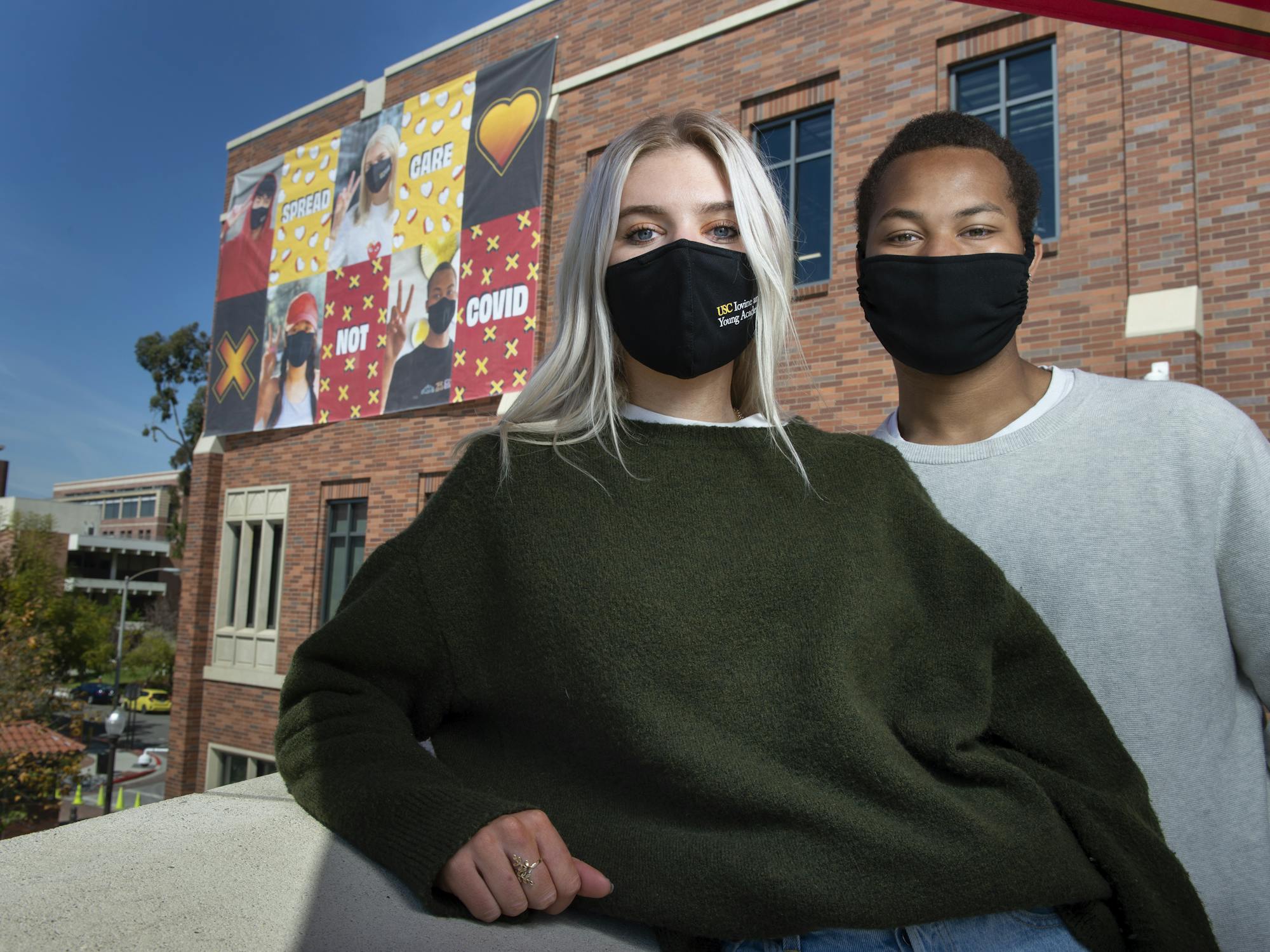 Two students wearing masks in front of building