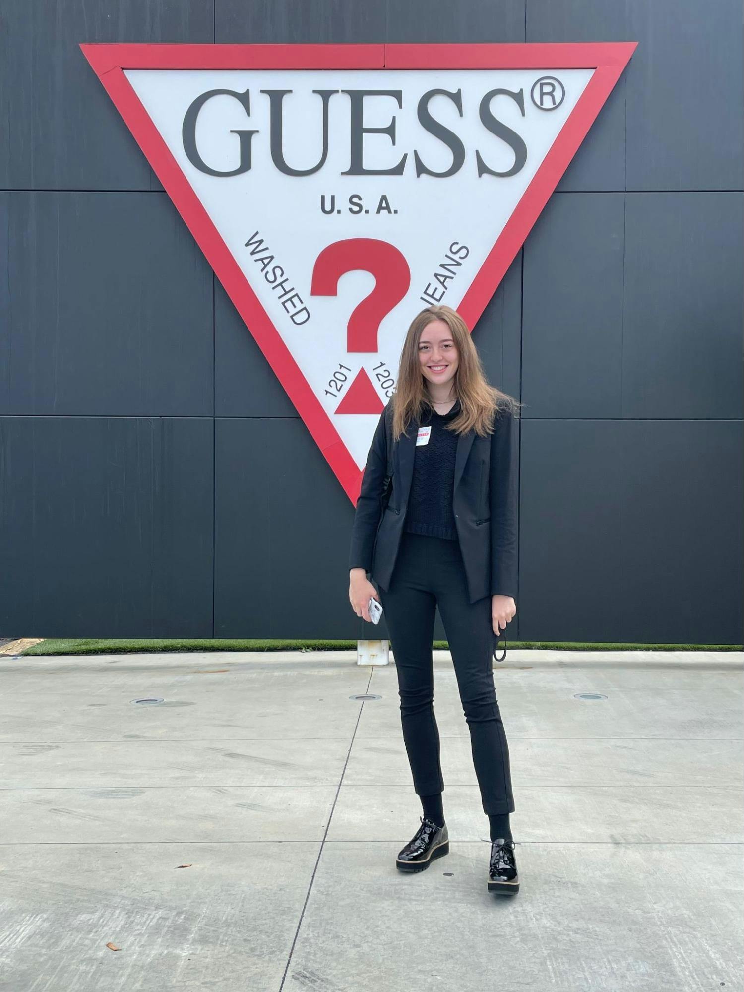 A young woman poses in front of a Guess sign