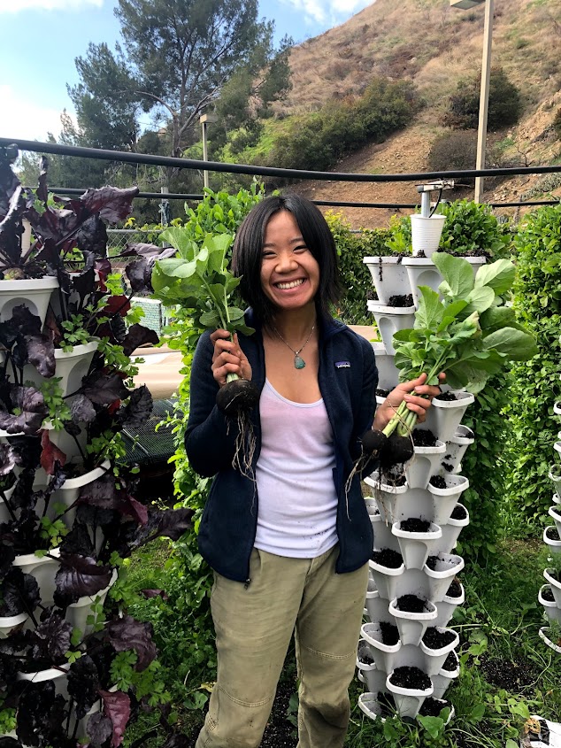 Erika Hang smiling and holding plants in a garden.