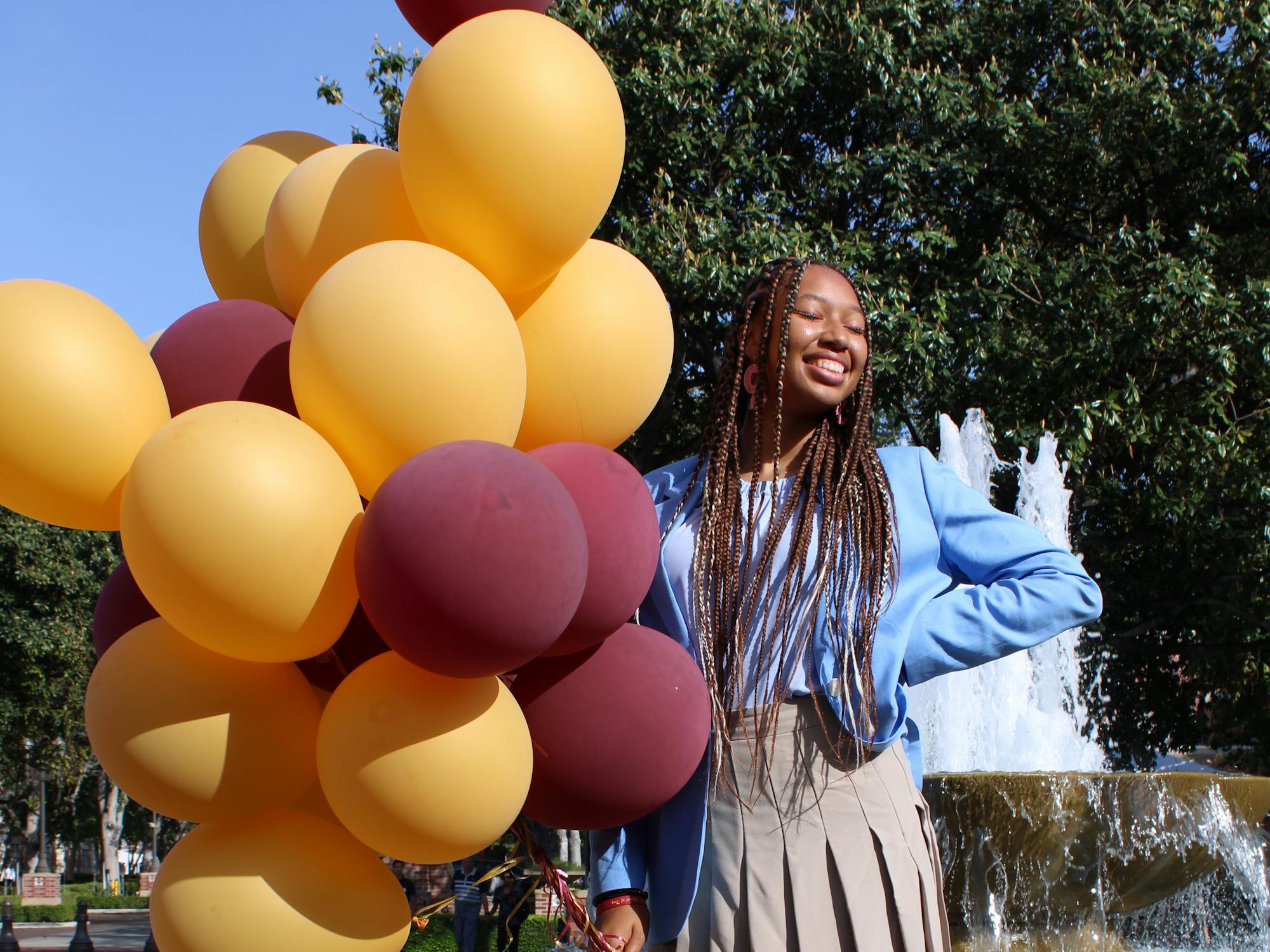 A person smiles with balloons in front of a fountain