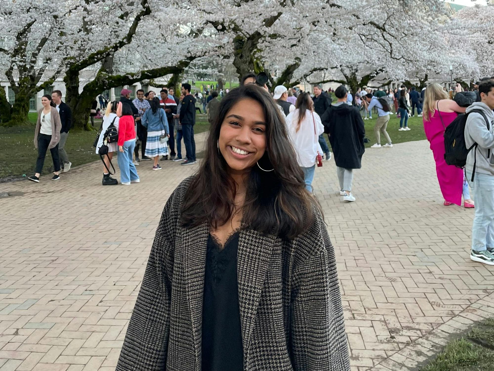 A young woman poses in front of a cherry blossom tree with people behind her
