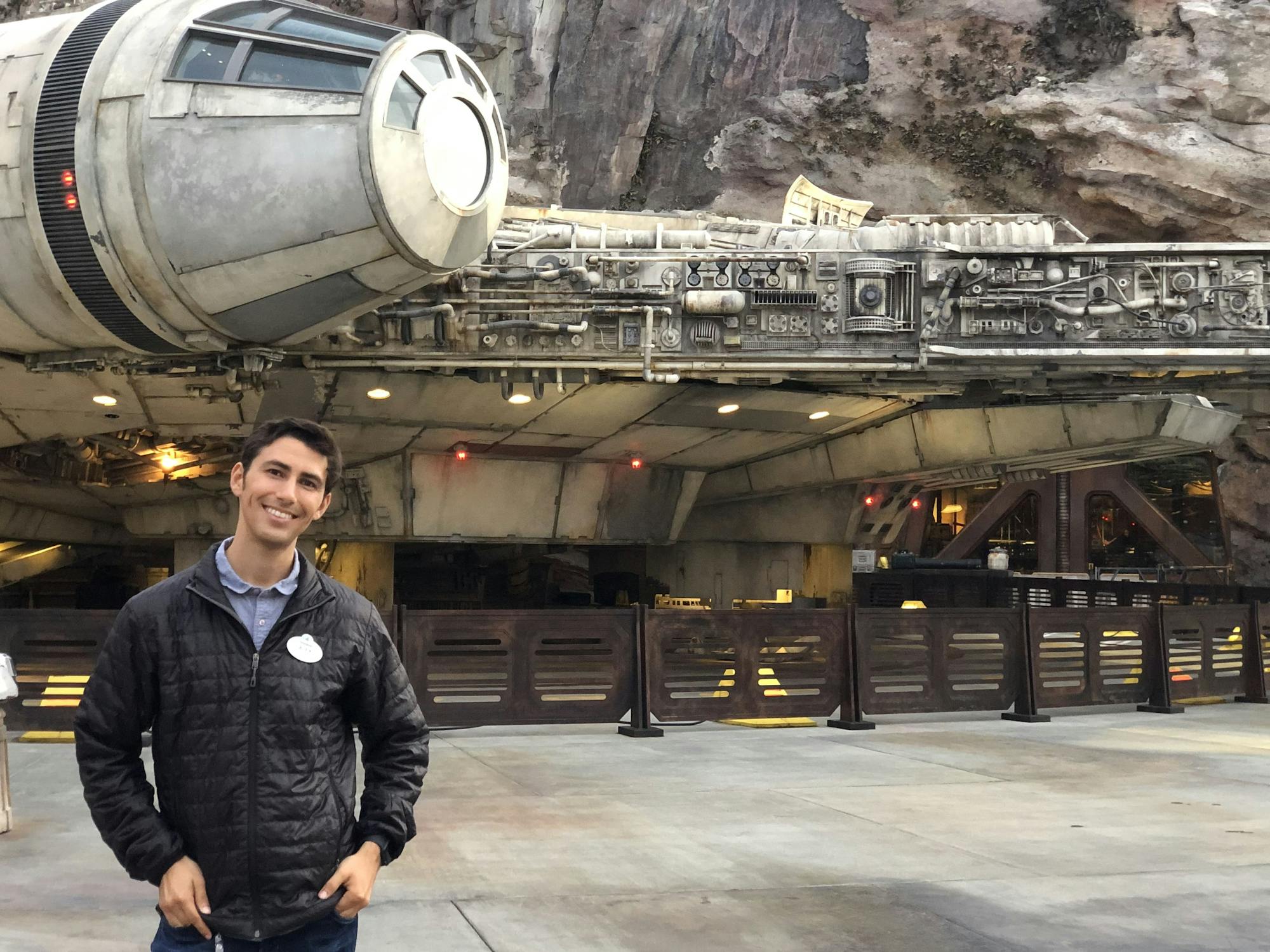 A young man smiles next to a Disneyland recreation of the Millennium Falcon from Star Wars
