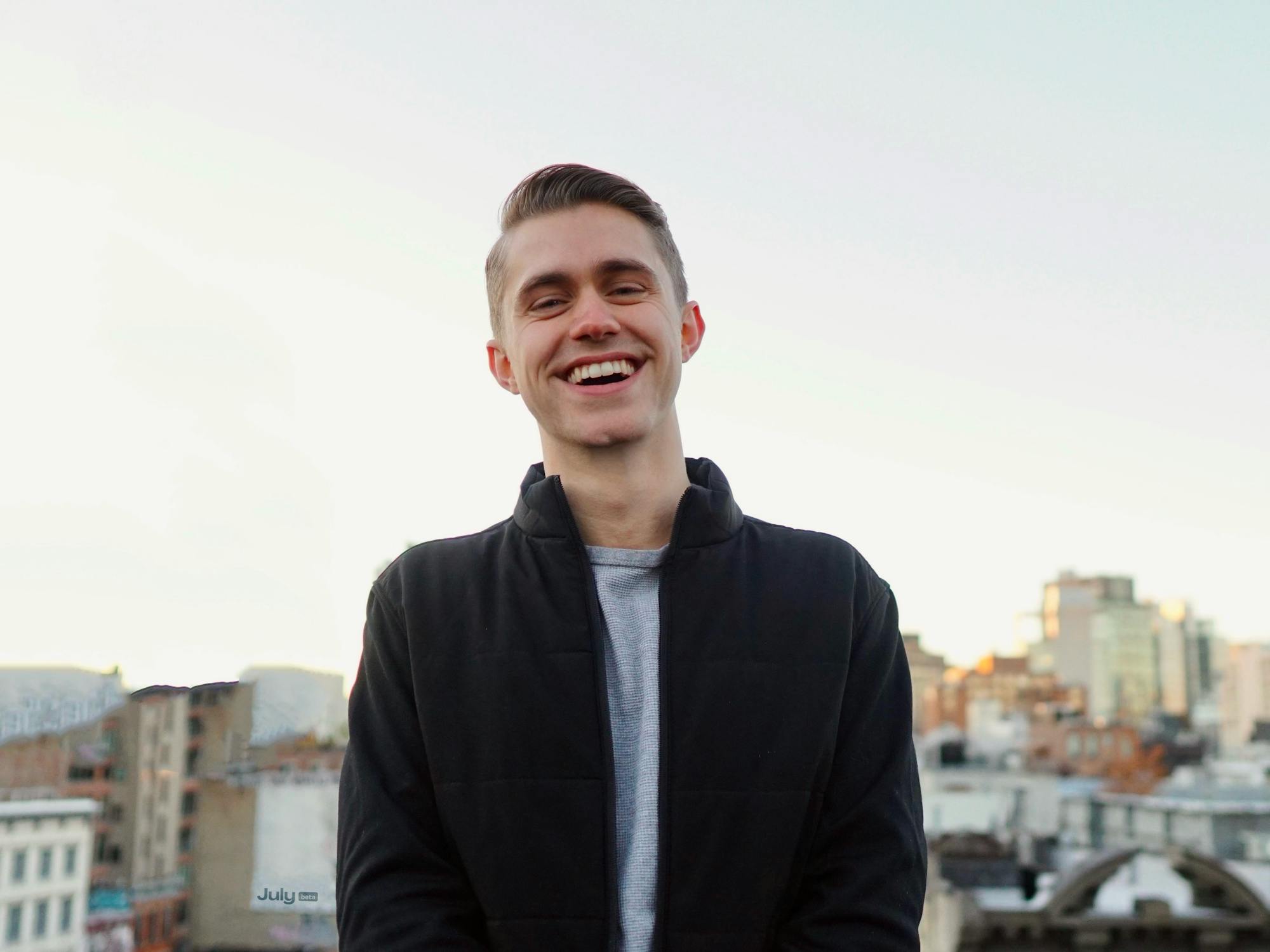 A person smiles on a roof in a black jacket