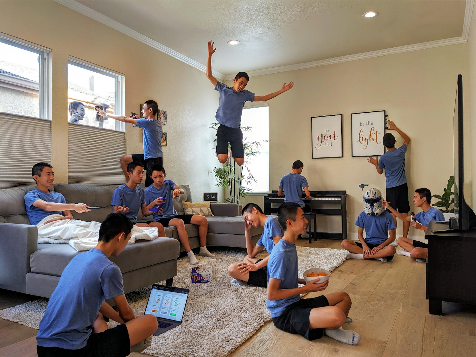 Multiples same young man in a blue t-shirt and dark shorts are superimposed performing various activities in a living room: typing on a laptop on the floor, jumping off a couch, wearing a stormtrooper helmet, and so on.