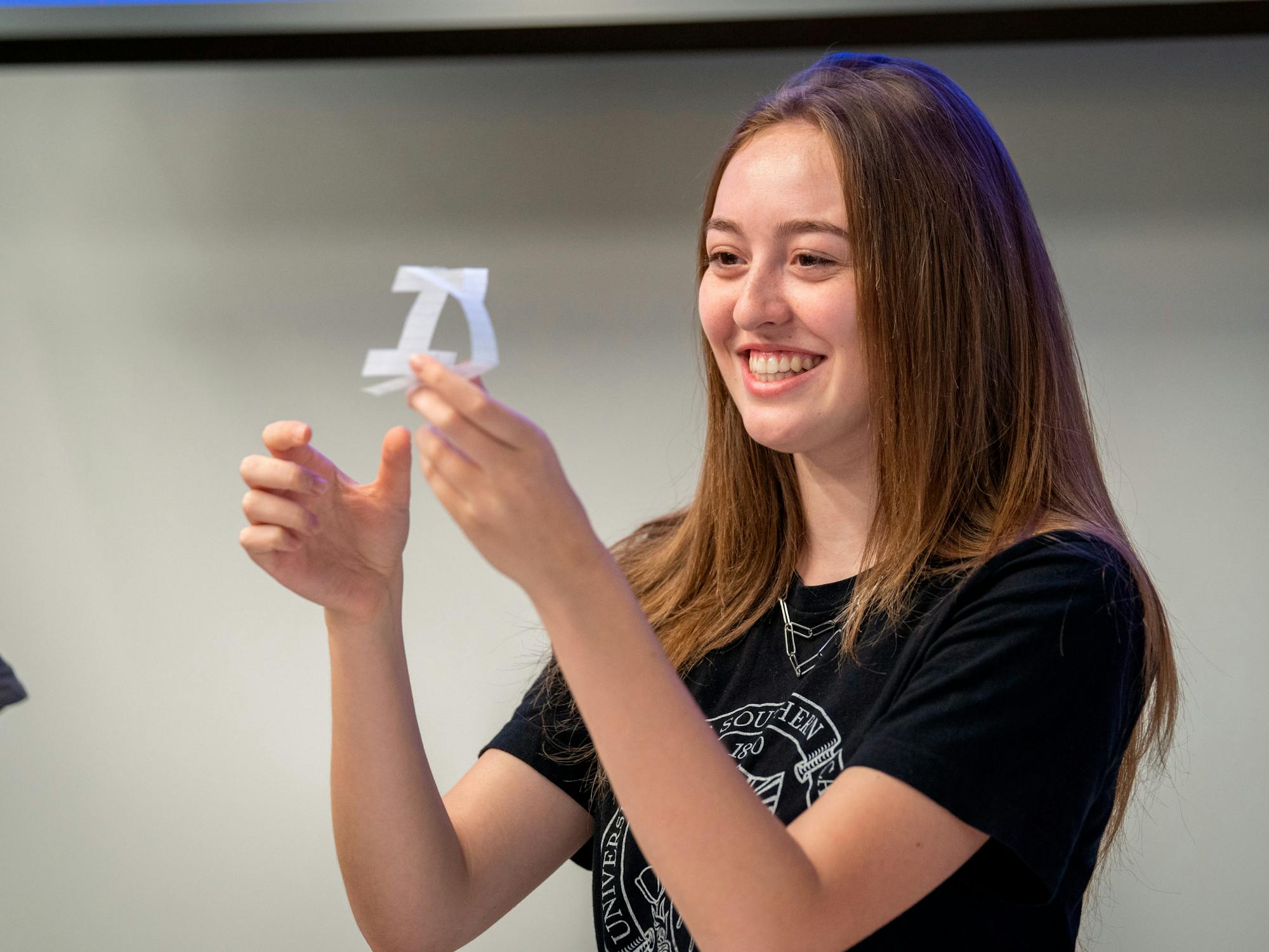 A young woman grins at a delicate cut-paper craft she holds