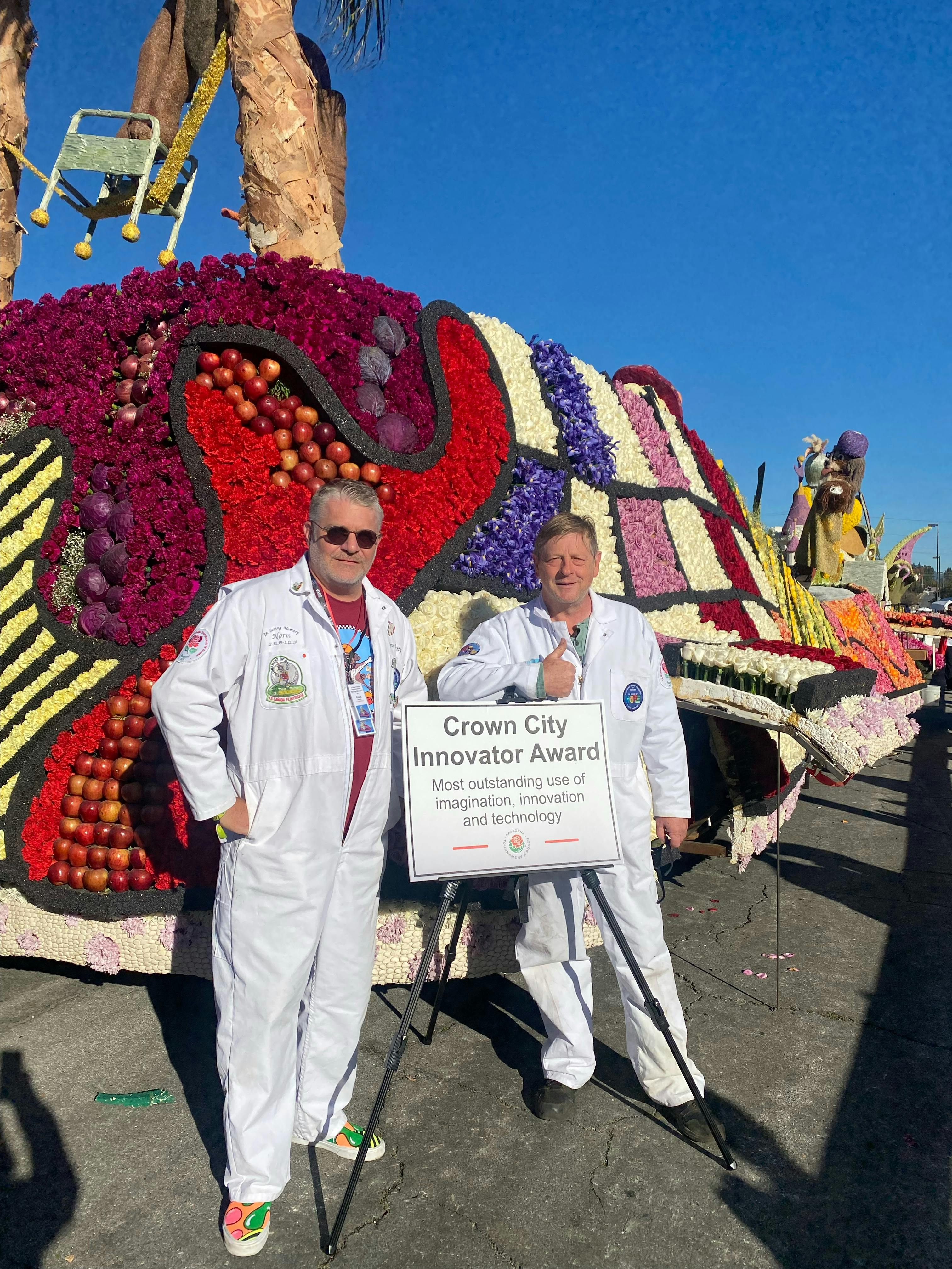 Two men post in front of parade float with Crown City Innovator Award