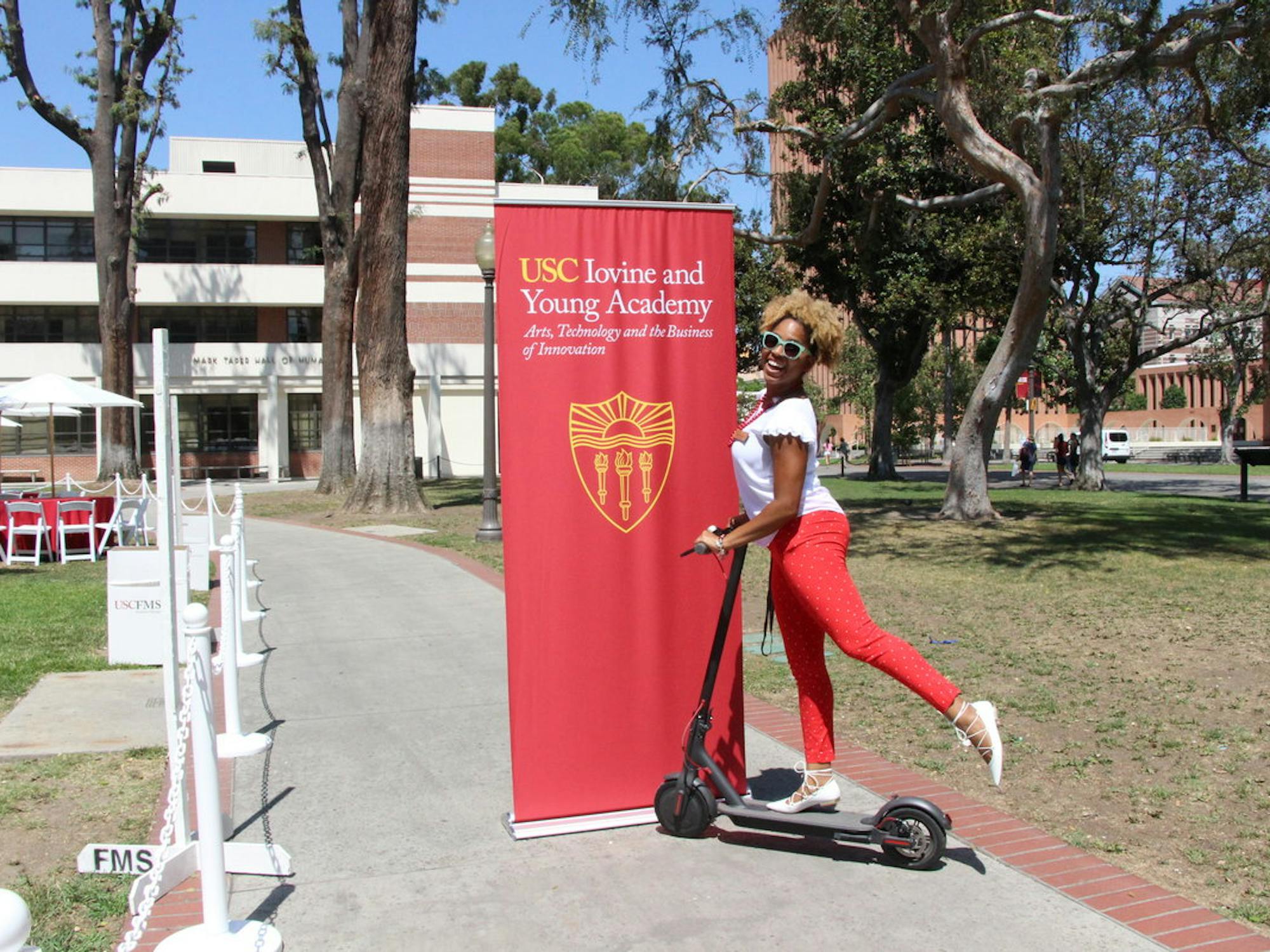 A woman poses atop a scooter near a banner that reads USC Iovine and Young Academy