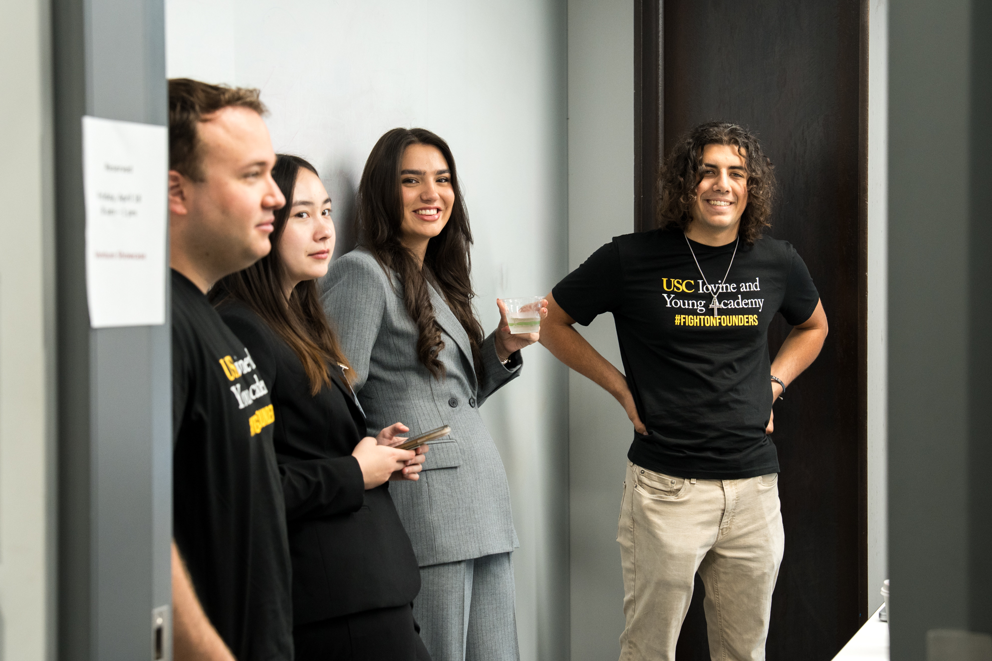 Four students stand in a conference room. One's shirt is clearly visible. It says "USC Iovine and Young Academy #fightonfounders".