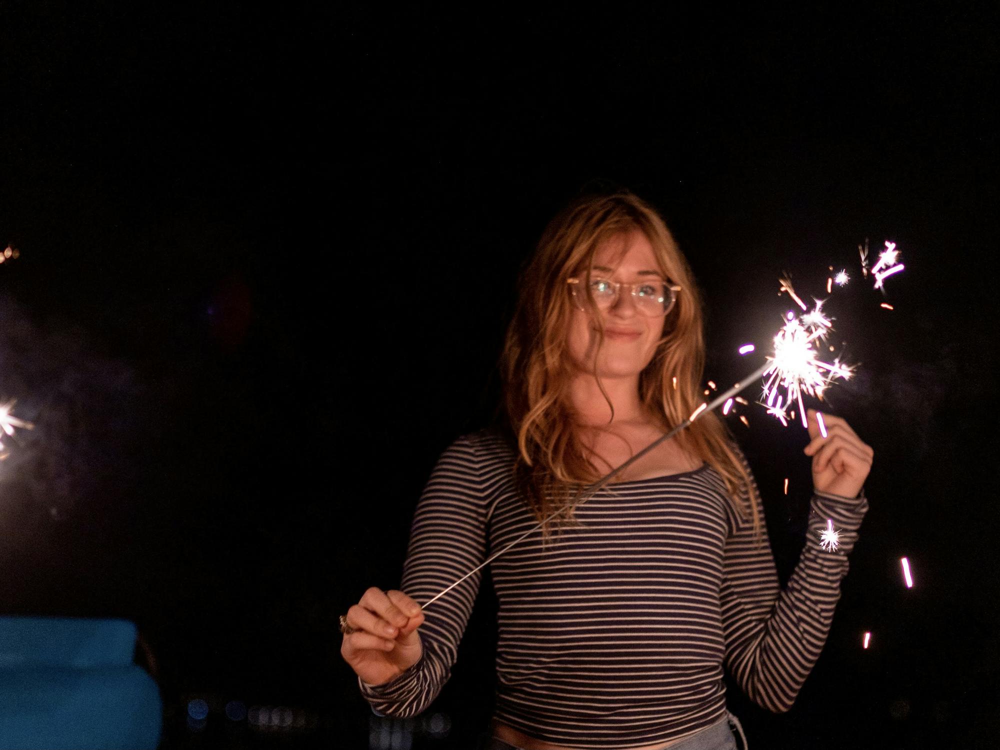 A young woman in the dark grins at the firework sparker in her hand