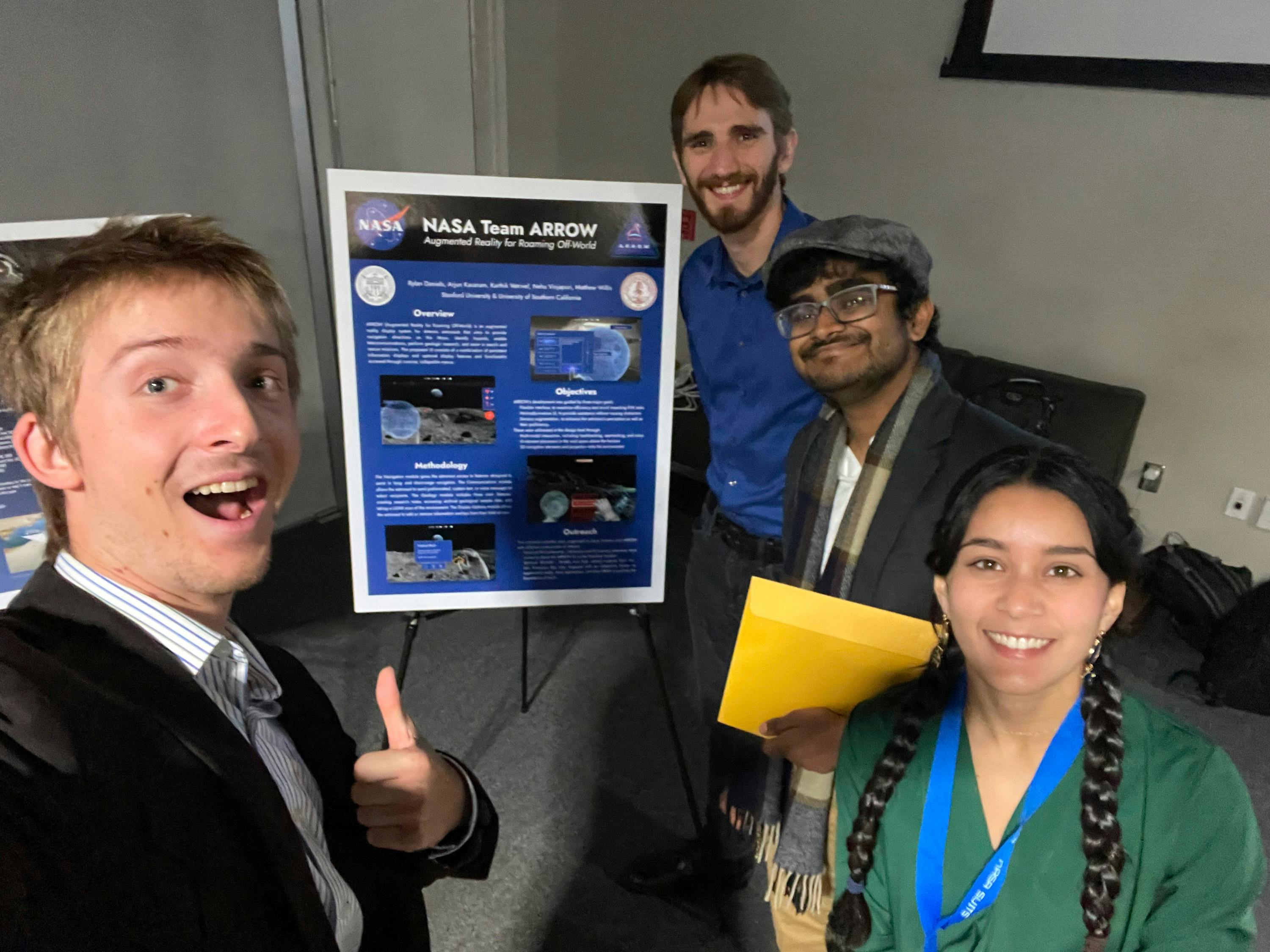 Selfie of a group of four young people smiling near a poster that reads "NASA Team ARROW"