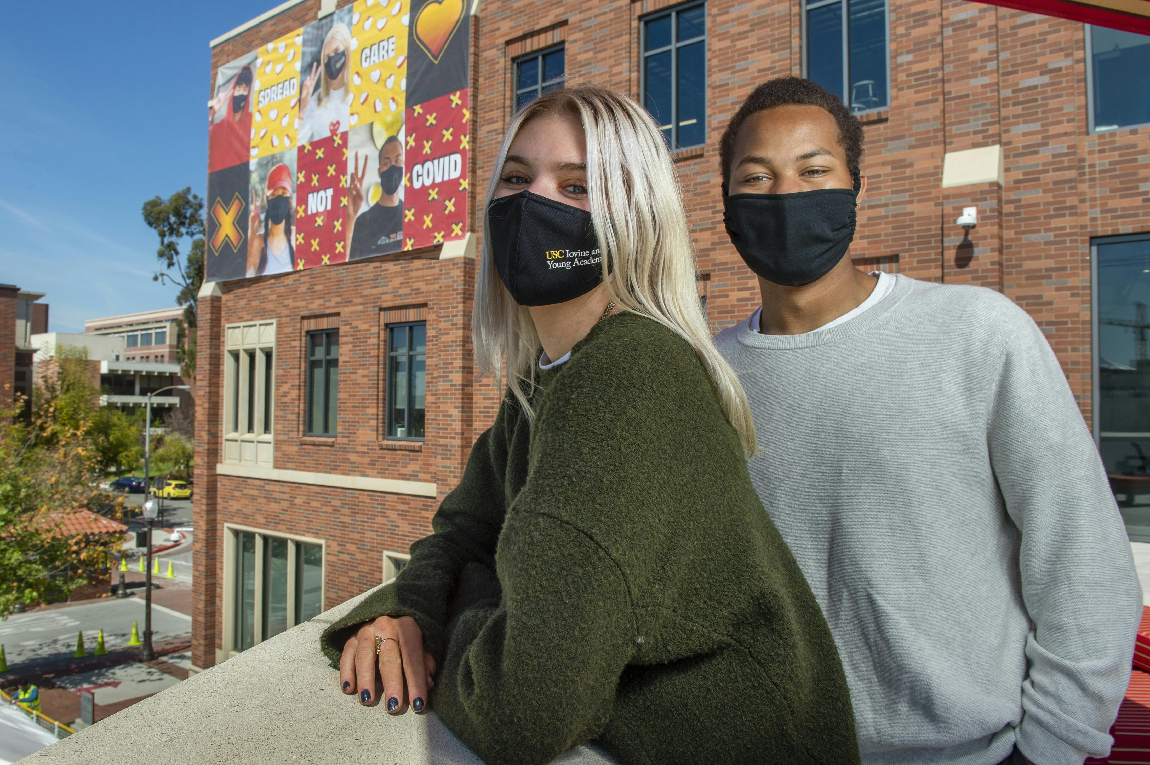 Two masked students in front of building with banner signage