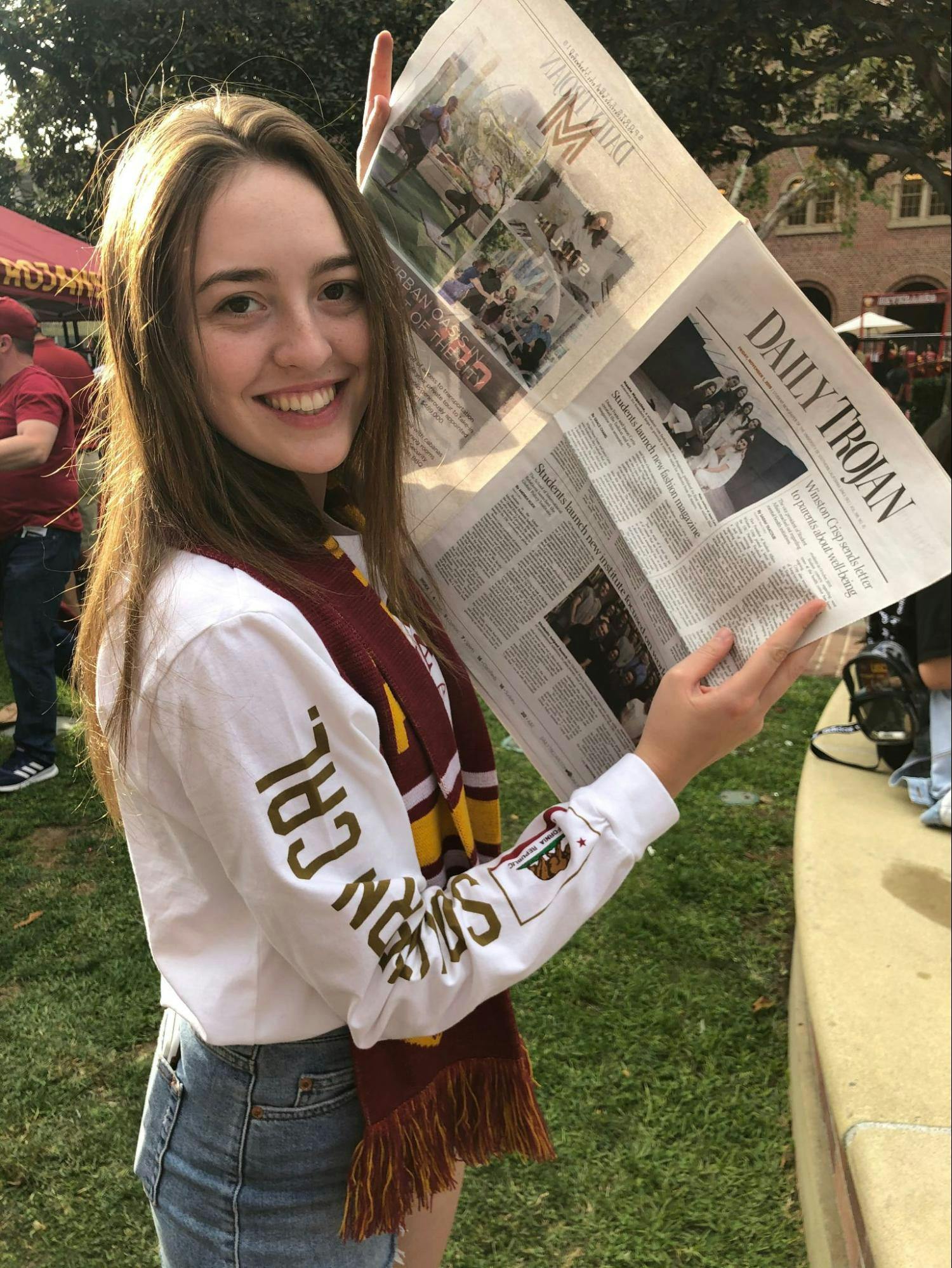 A young woman in USC clothes holds up a copy of the Daily Trojan