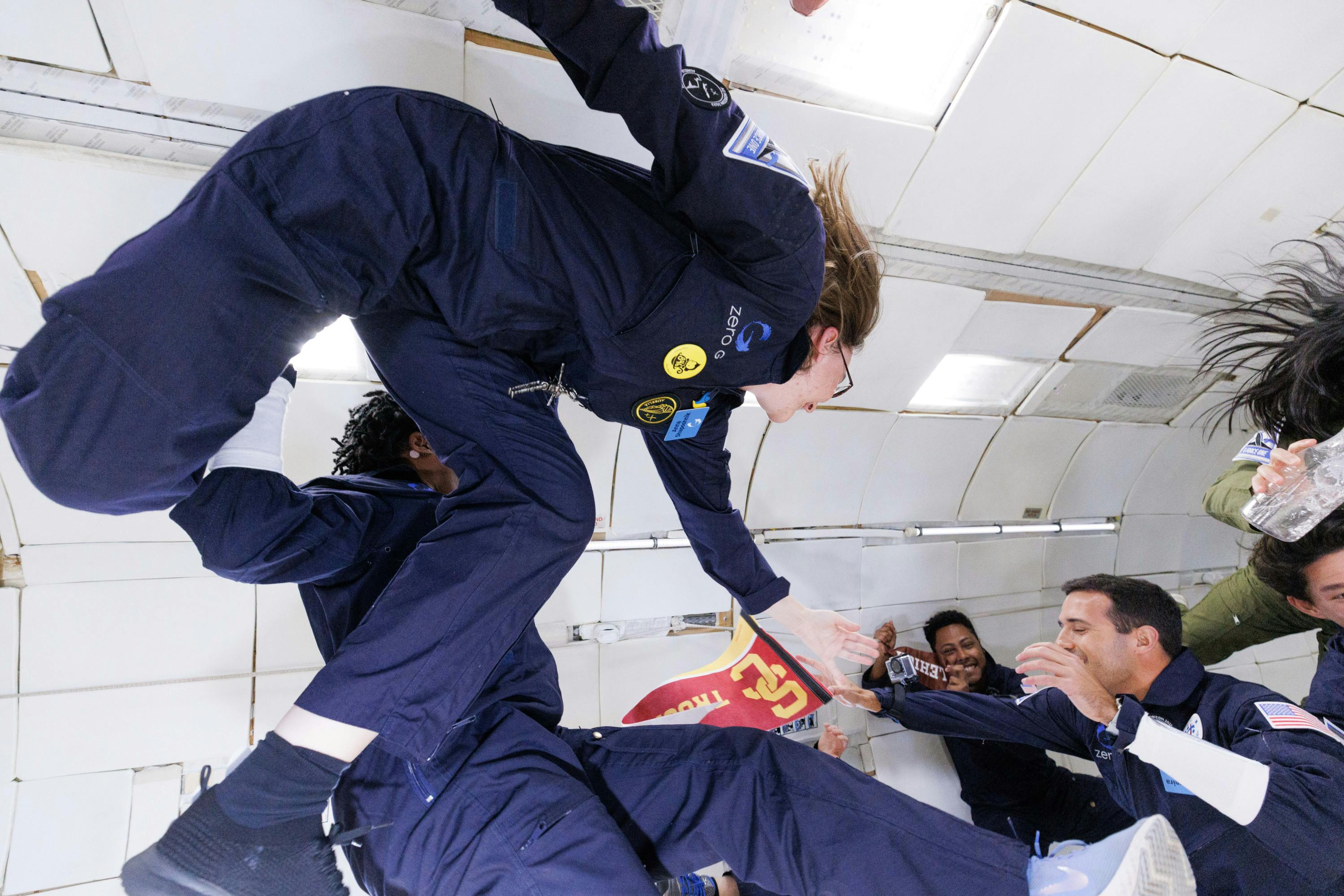A young woman floats in zero gravity in a flight suit, posing for camera