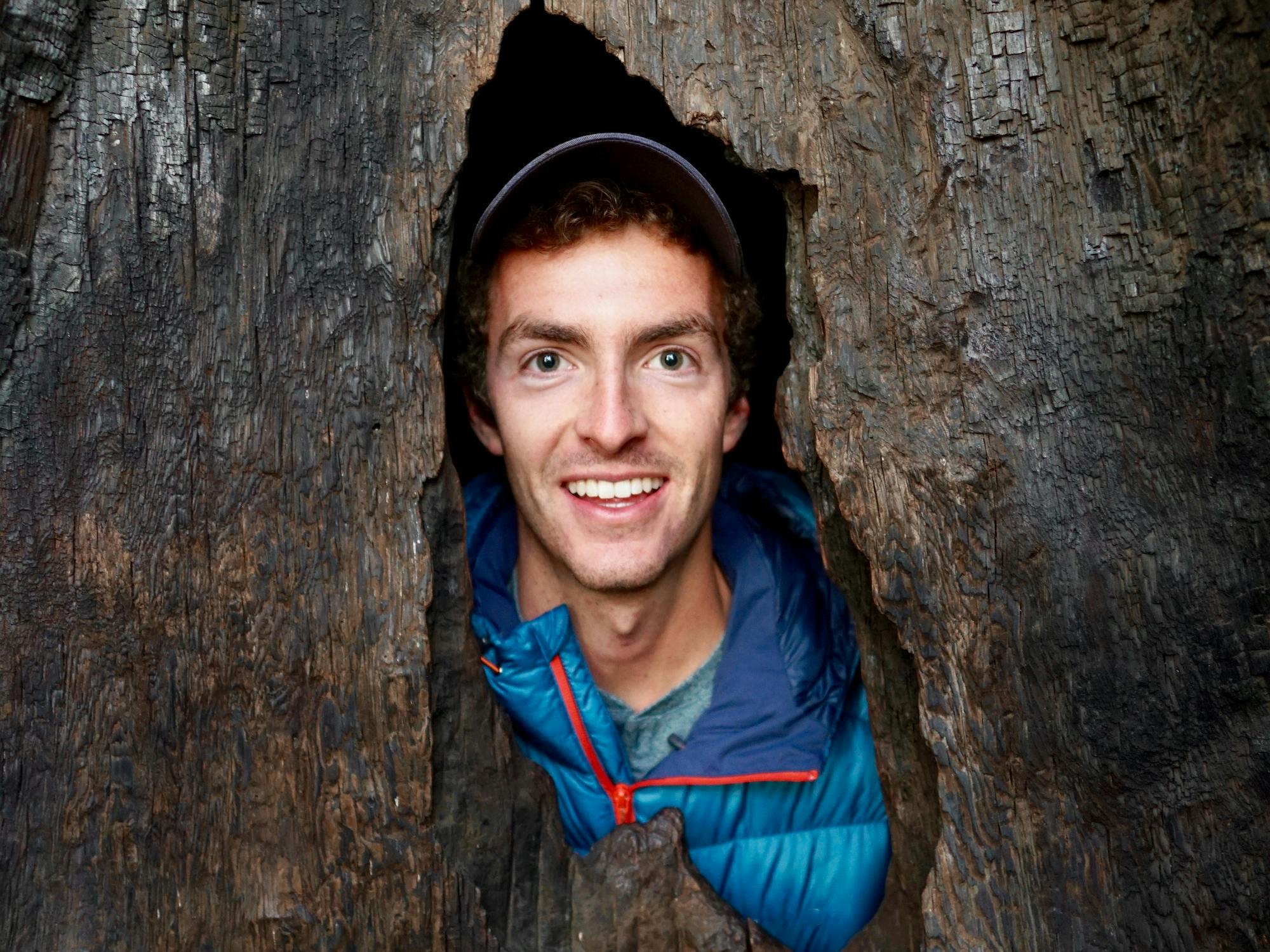 Smiling male peering through tree trunk