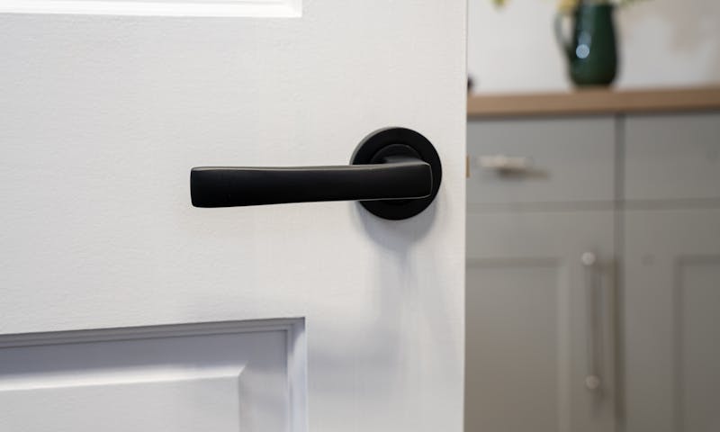 An image of a black door handle on a white door