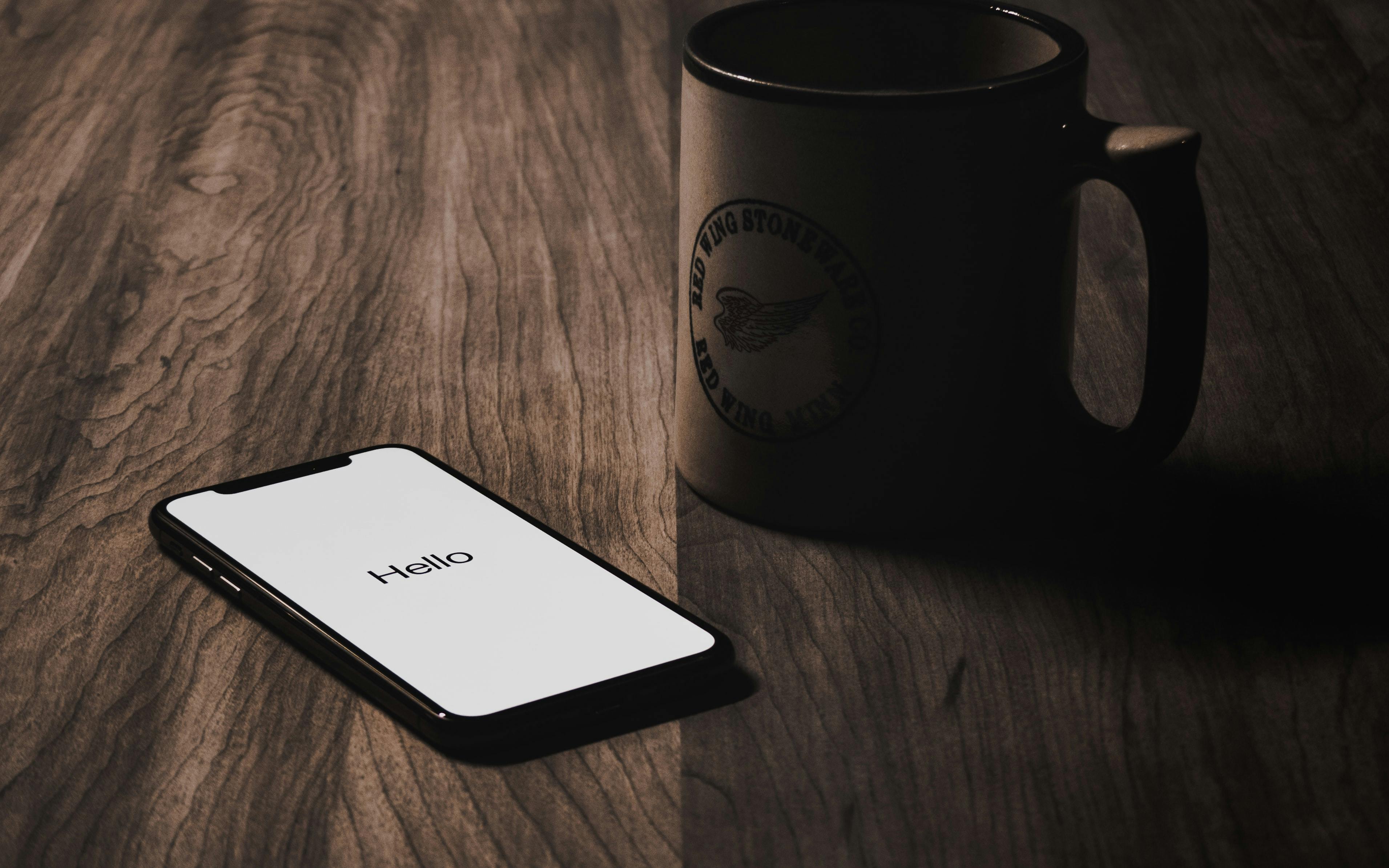 iPhone with 'Hello' onscreen and coffee cup lying on table