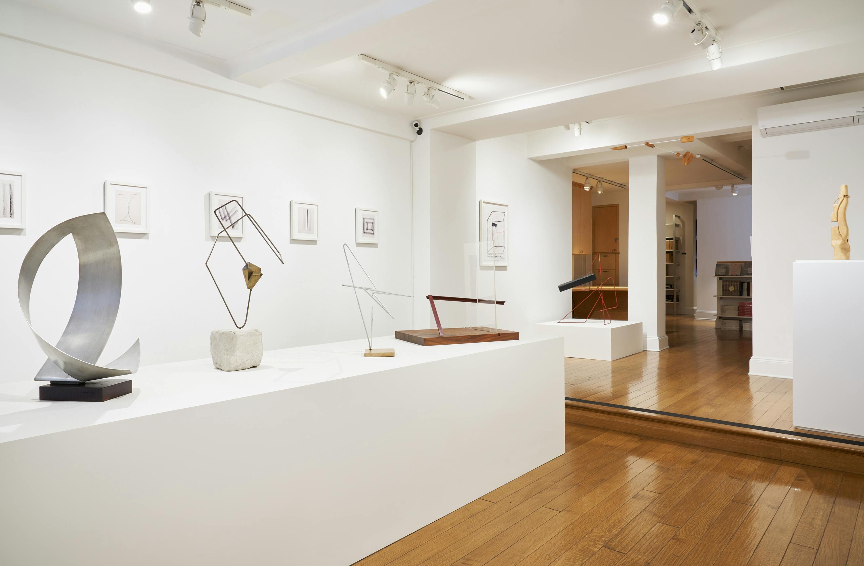 Gallery view of From Surface to Space exhibition depicting one hanging sculpture, five free-standing sculptures, and six wall-mounted drawings.